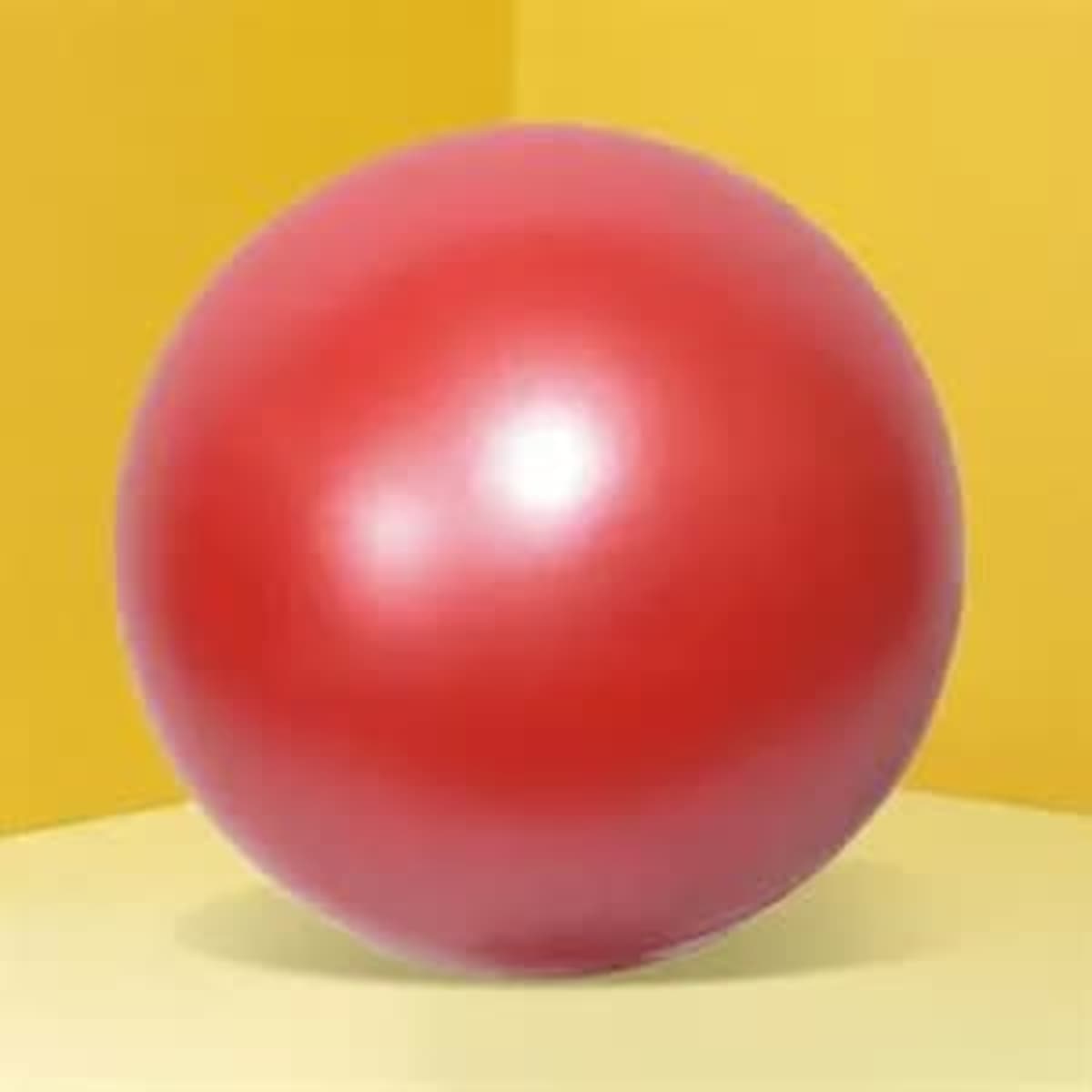 A shiny red stress ball on a yellow and light yellow backdrop, featuring a smooth surface and round shape.