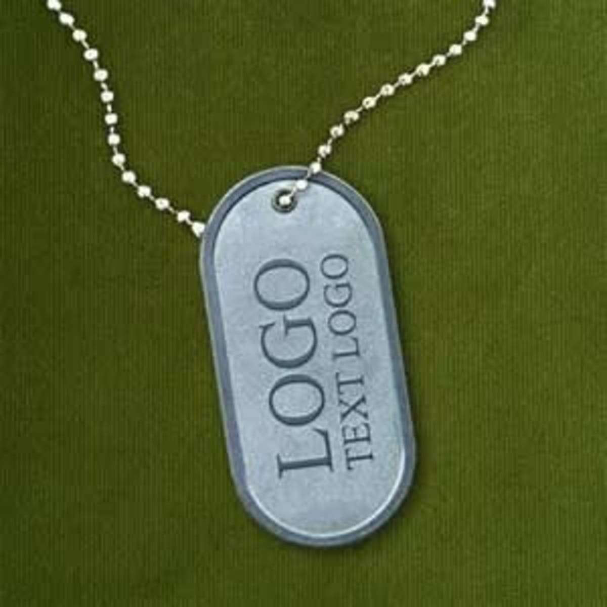A die-struck dog tag in grey metal hanging from a silver ball chain on a green background.