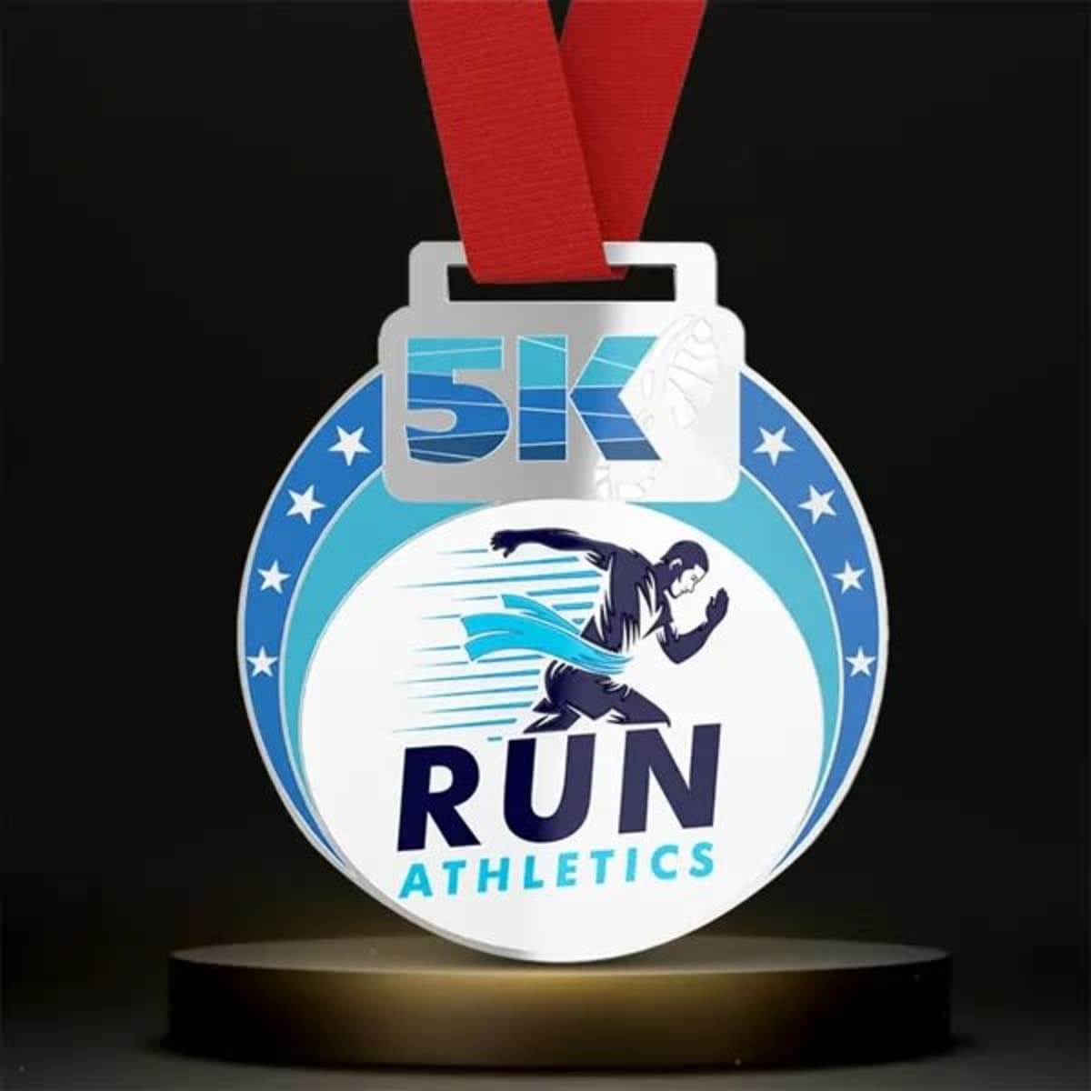 A round, silver medal featuring red ribbon, blue accents, and an image of a runner with "5K" and "RUN ATHLETICS" text.