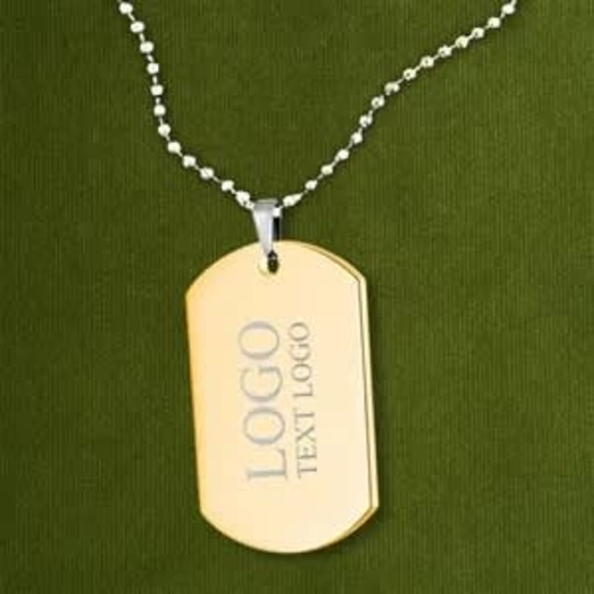 A stainless steel dog tag in gold, hung on a silver ball chain, resting against a dark green background.