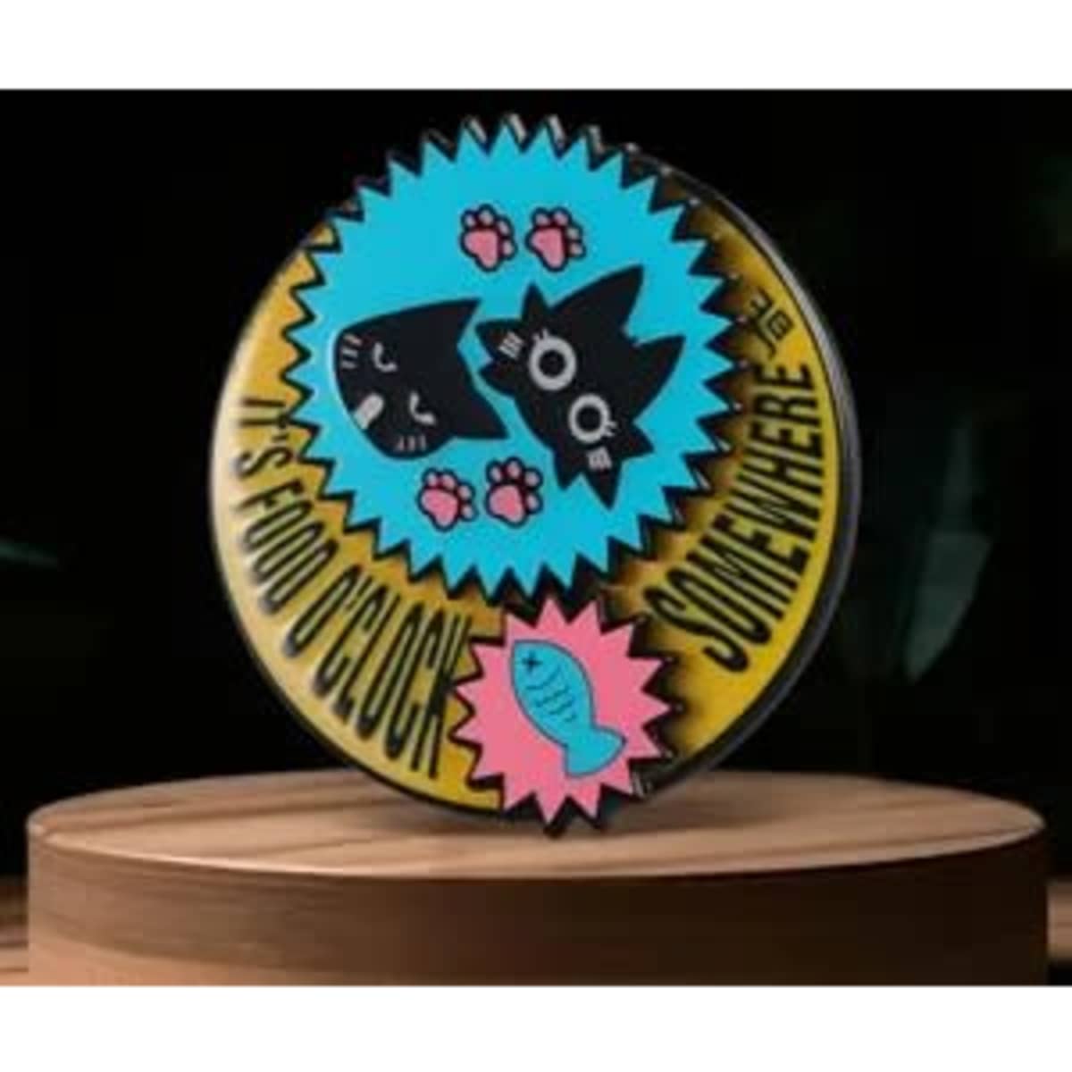 A colourful pin featuring two black cats, pink paw prints, and a fish, set against a bright blue background.