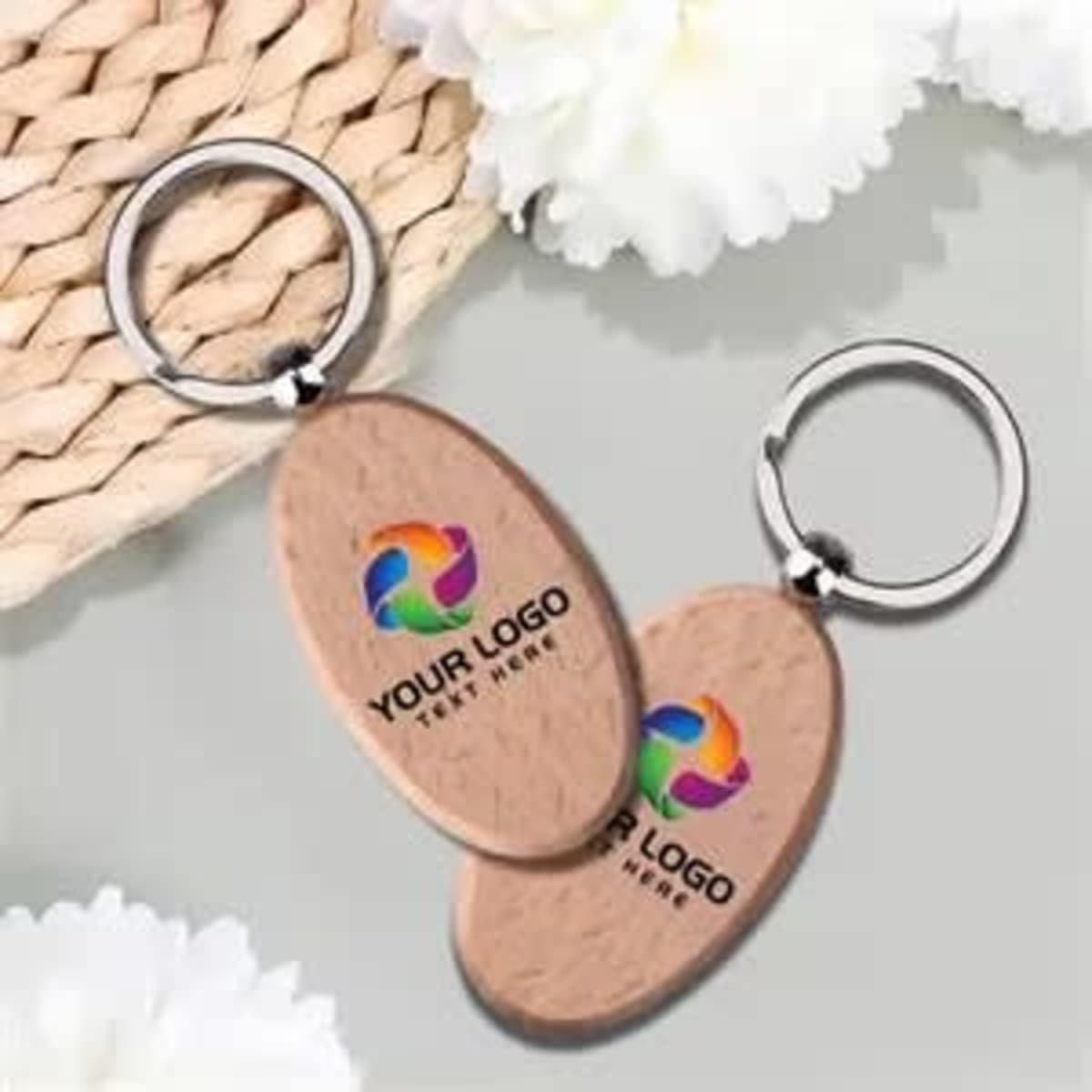 An oval wooden key holder featuring a silver keyring and a logo, set on a neutral background with white flowers.