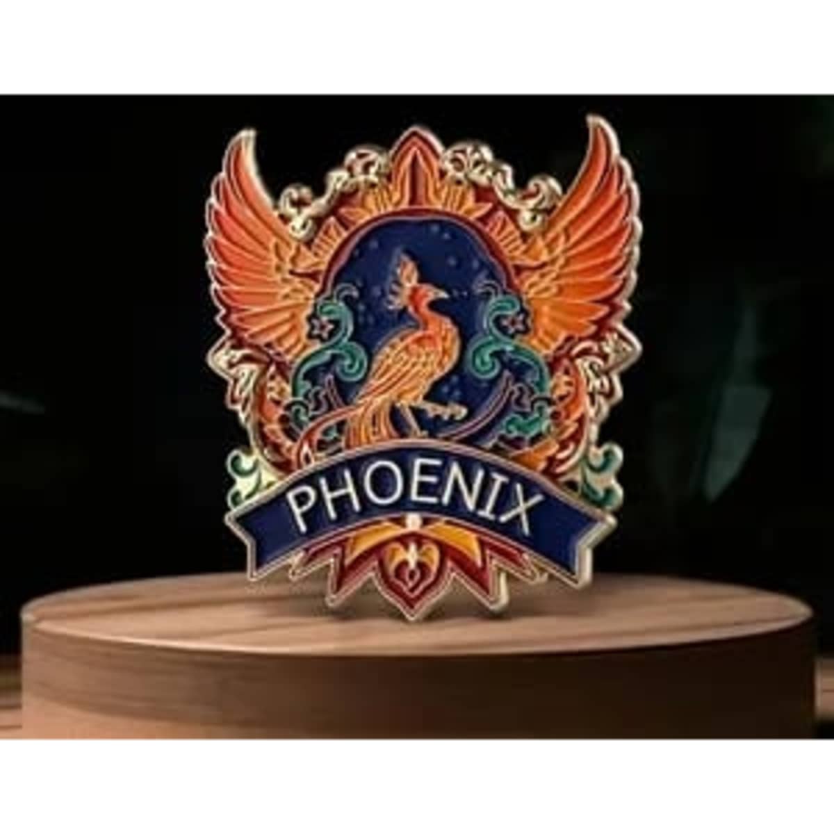 A layered standing pin featuring a vibrant phoenix design with orange and blue details, displayed on a wooden base.