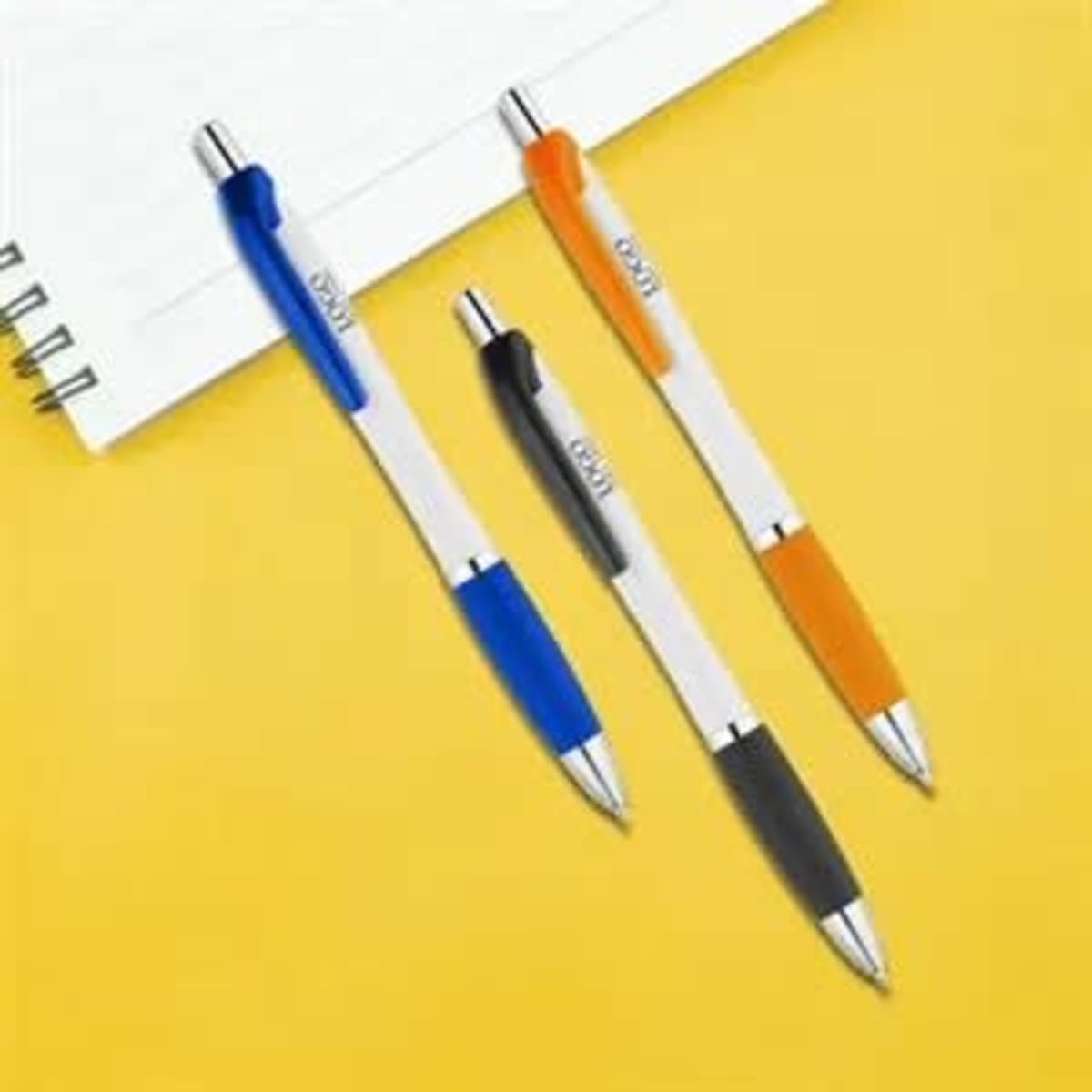 Three plastic ballpoint pens in blue, orange, and black, resting beside a notepad on a yellow background.