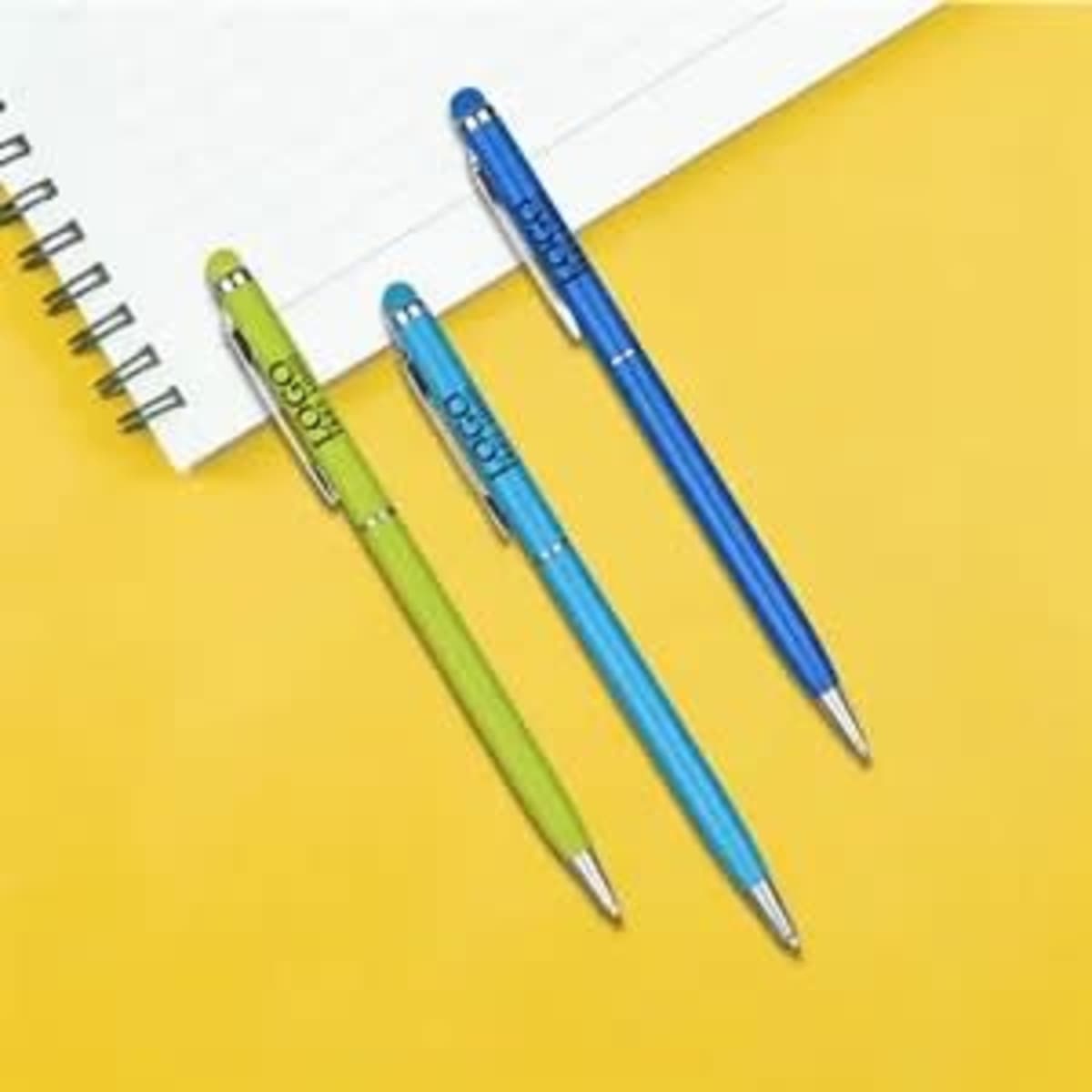 Three slim metal stylus pens in green, blue, and blue, placed beside a notepad on a yellow background.