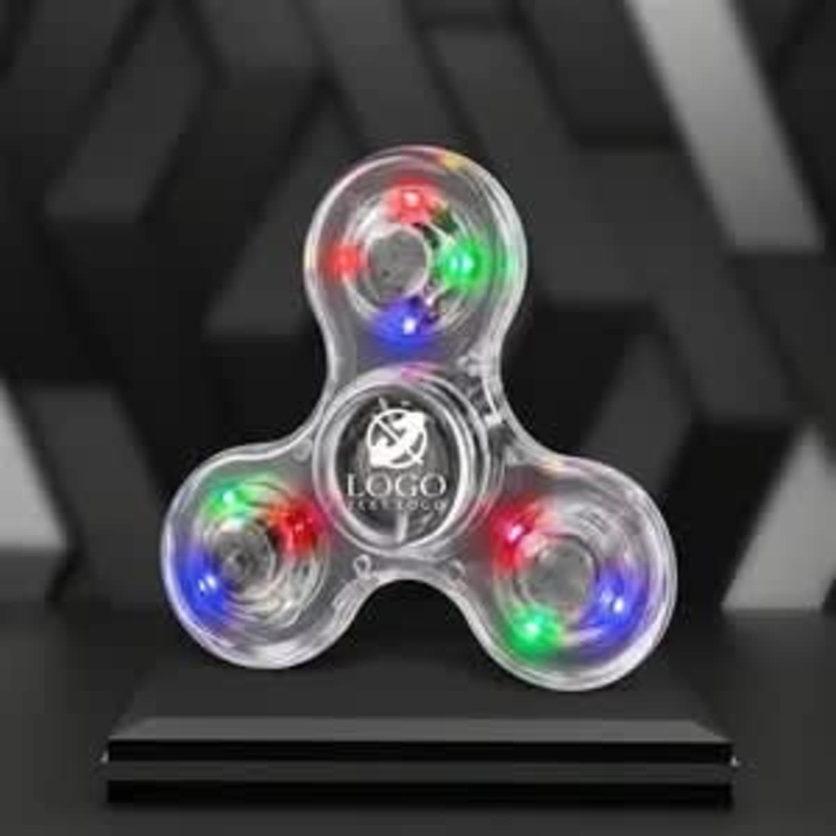 A clear LED light fidget spinner with red, green, and blue lights, featuring a logo on its centre.