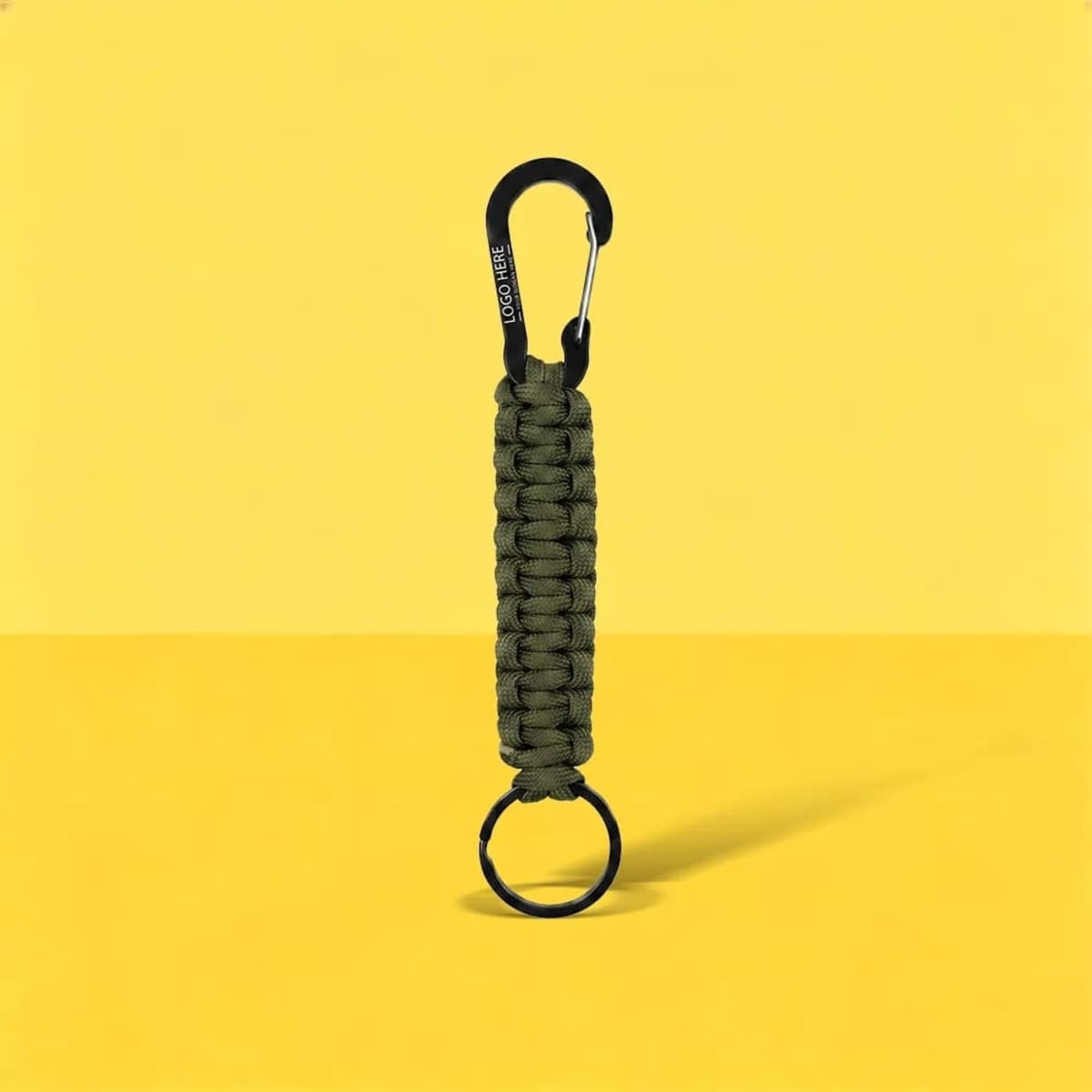 An olive green paracord keychain with a black carabiner and a metal keyring, set against a yellow background.