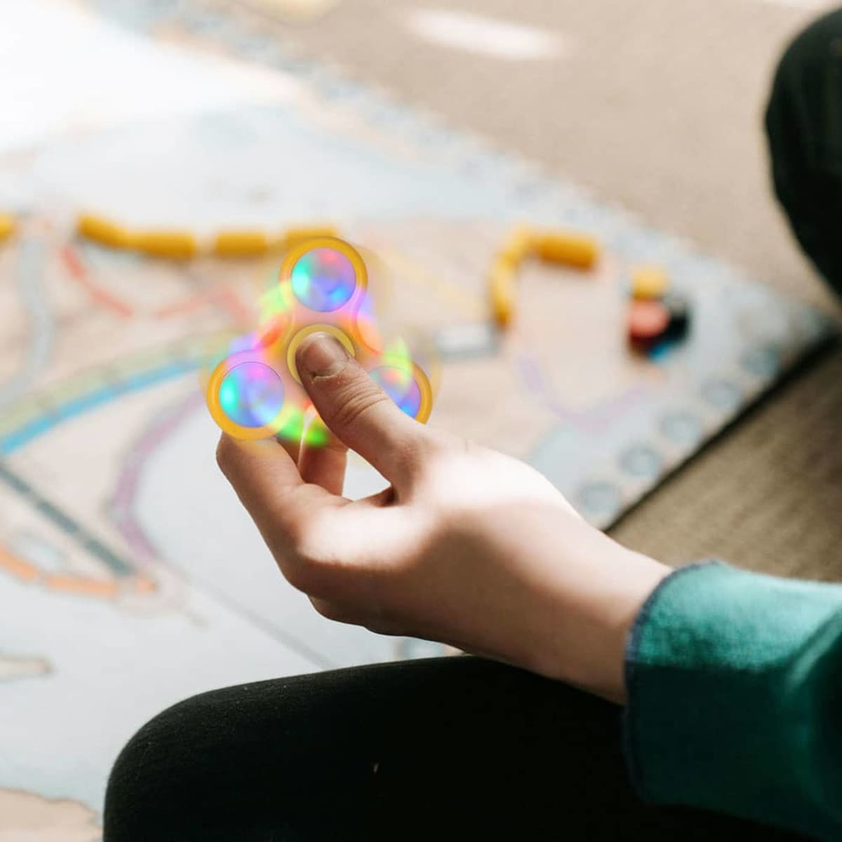 A hand holding a multicoloured LED fidget spinner with a game board featuring circular tokens in the background.