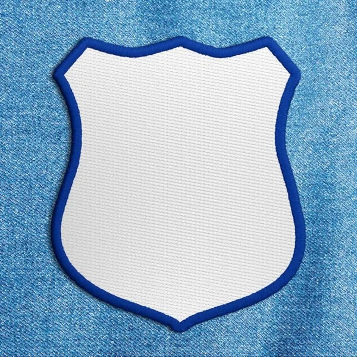 A blank shield-shaped patch in white with a blue border on a textured blue background.