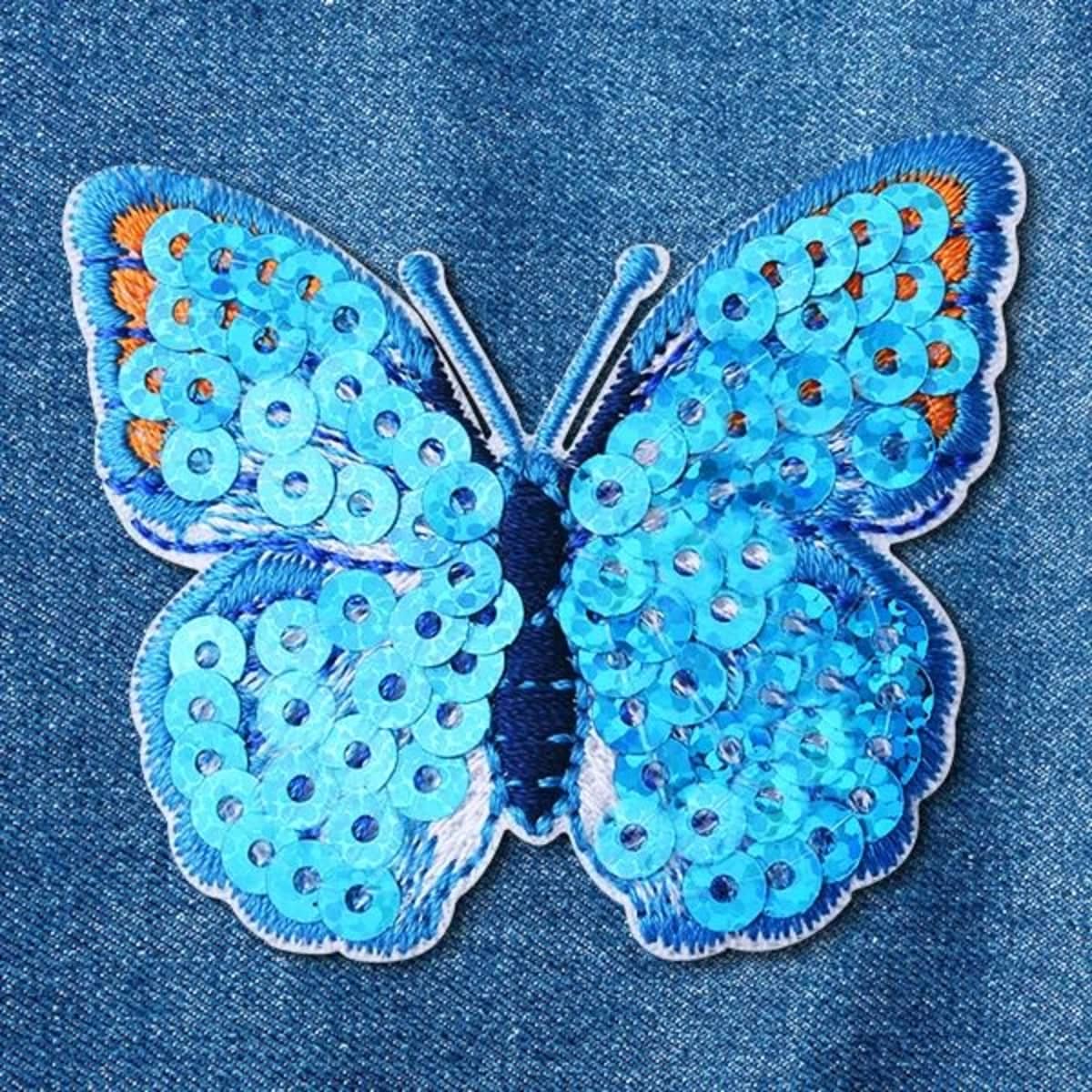 A blue sequin butterfly patch with varying tones of blue and sequins, stitched onto a denim background.