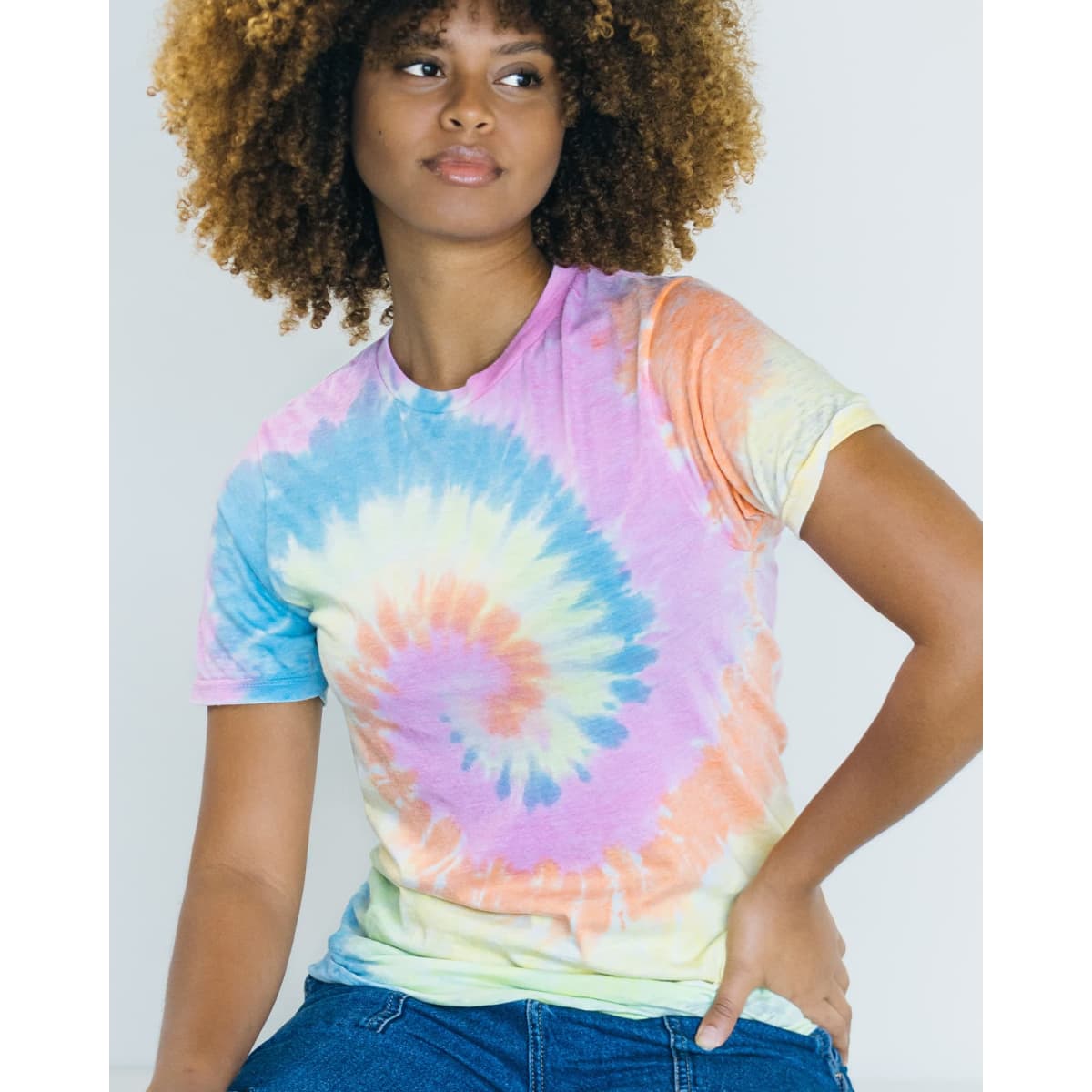 A woman models a Colortone® tie dye adult T-shirt featuring a spiral pattern in pastel colours of blue, pink, yellow, and green.