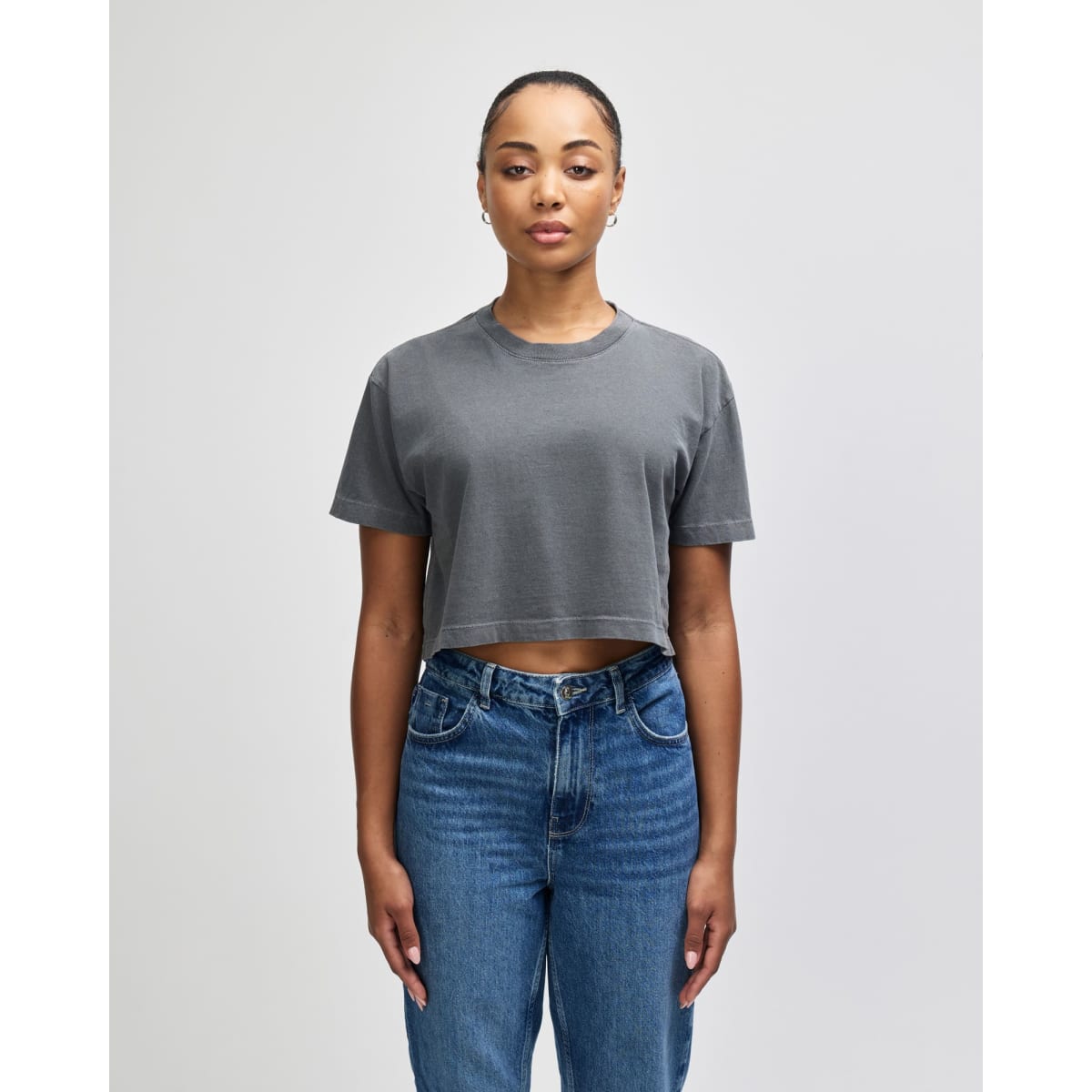 A grey crop boxy T-shirt in heavyweight cotton, featuring a relaxed fit and short sleeves. The model wears blue jeans.