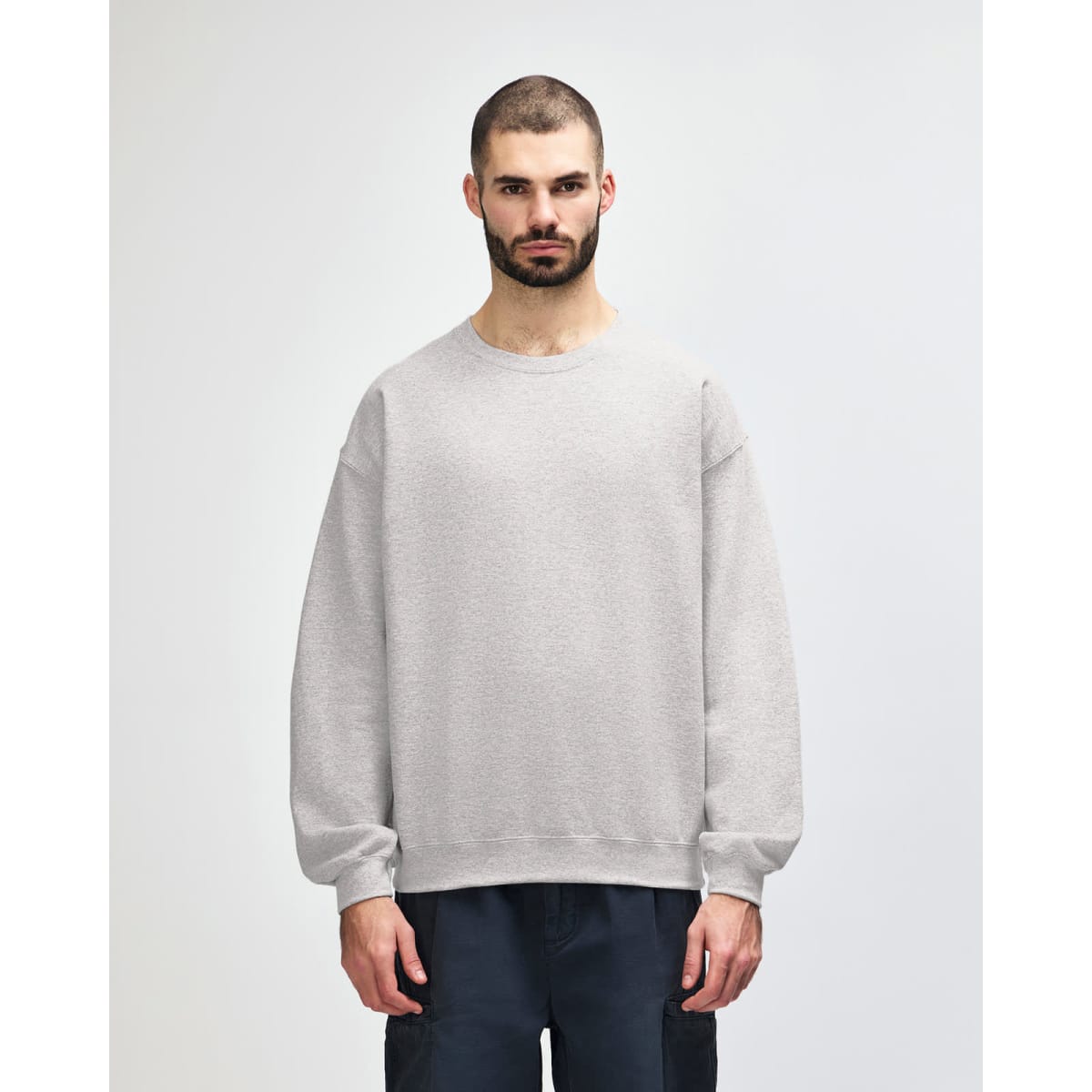 A grey Gildan Heavy Blend adult crewneck sweatshirt displayed on a model, featuring long sleeves and a comfortable fit.