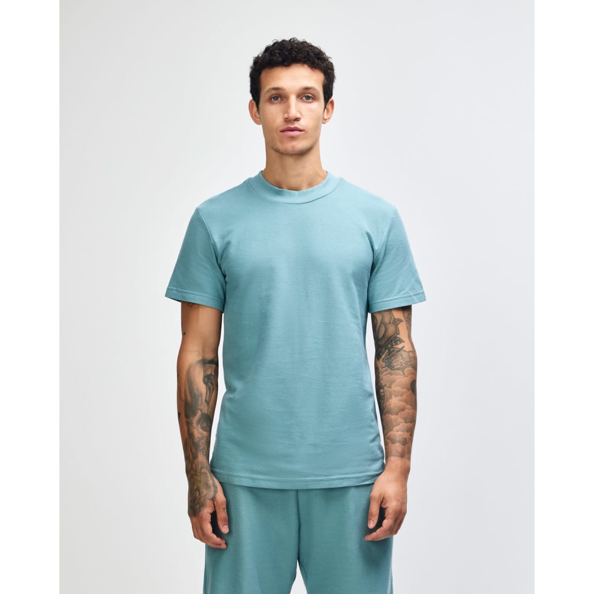 A unisex mockneck t-shirt in a soft green hue, featuring short sleeves and a relaxed fit. It has a logo on it.