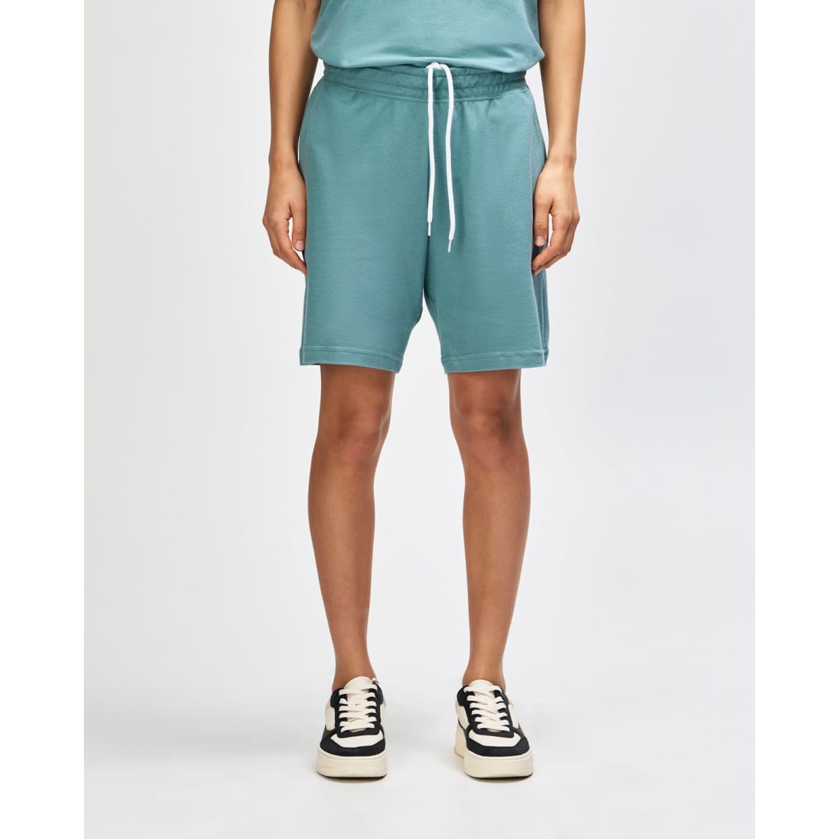 Unisex gym shorts in a soft teal colour, featuring an elastic waistband and pockets, paired with white sneakers.