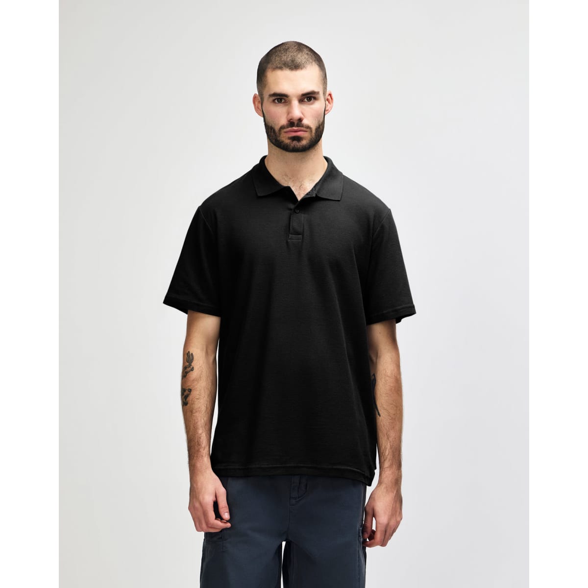 A model wearing a black Gildan Softstyle Adult Double Pique Polo with a logo on the chest.