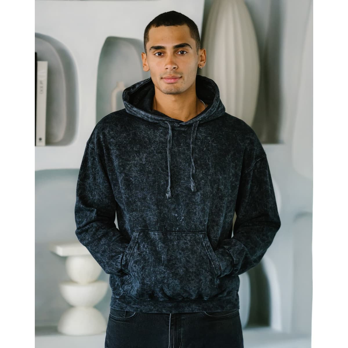 A man stands wearing a navy blue mineral wash pullover hoodie, featuring a front pocket and adjustable drawstrings.