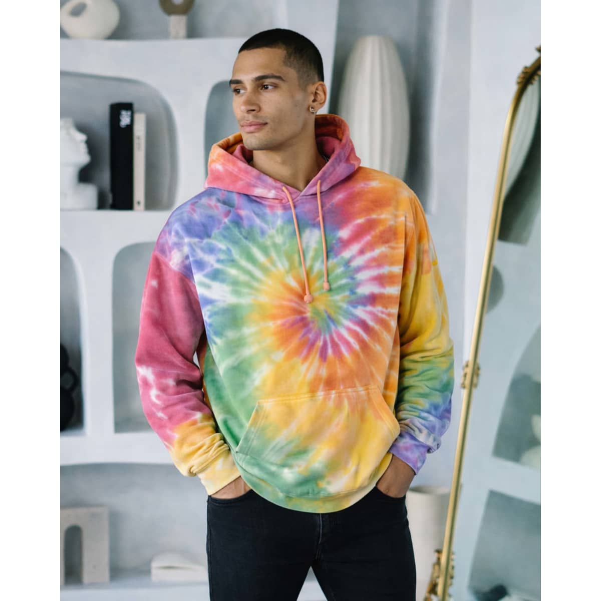 A hoodie in vibrant tie-dye colours of pink, yellow, green, and purple, worn by a young man. It has a front pocket and hood.