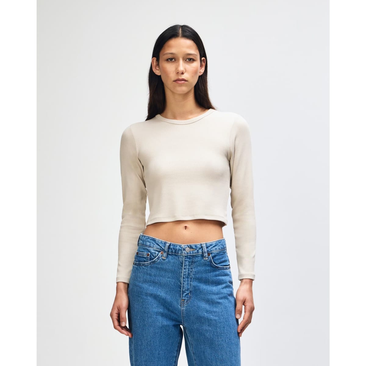 A fitted, long-sleeved crop t-shirt in a light beige colour, paired with high-waisted blue jeans.