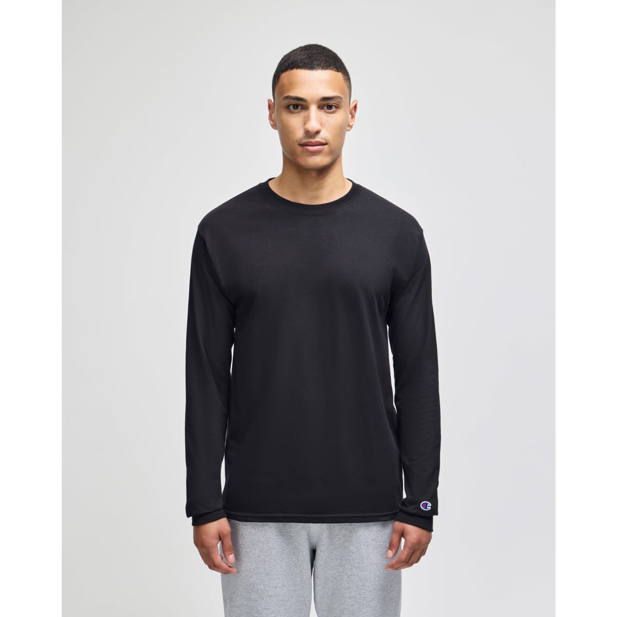 A black long-sleeve t-shirt with a logo, modelled by a person, paired with grey trousers.
