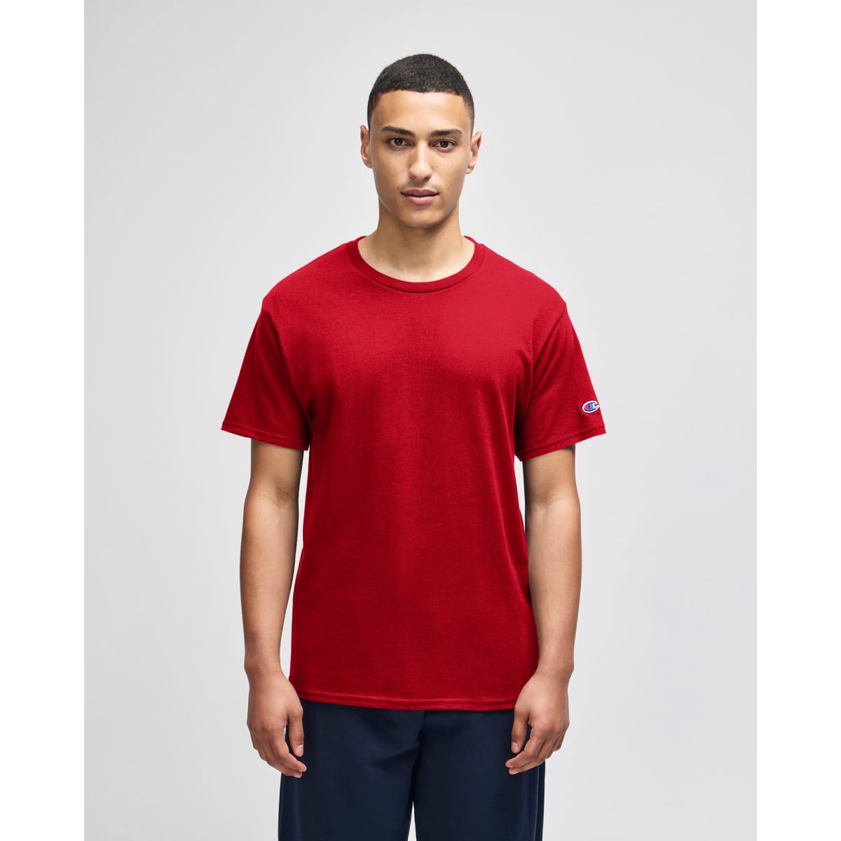 A red Champion adult jersey short sleeve t-shirt displayed on a model with a logo on the sleeve.