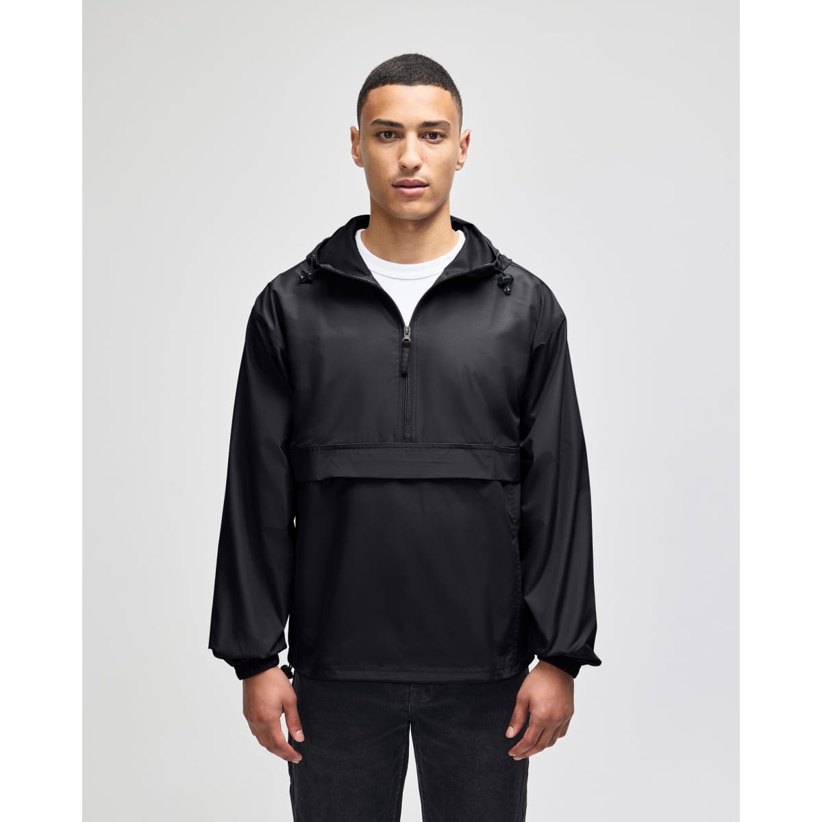 A black packable anorak jacket with a hood, featuring a front zip and a logo. Model is standing against a plain background.