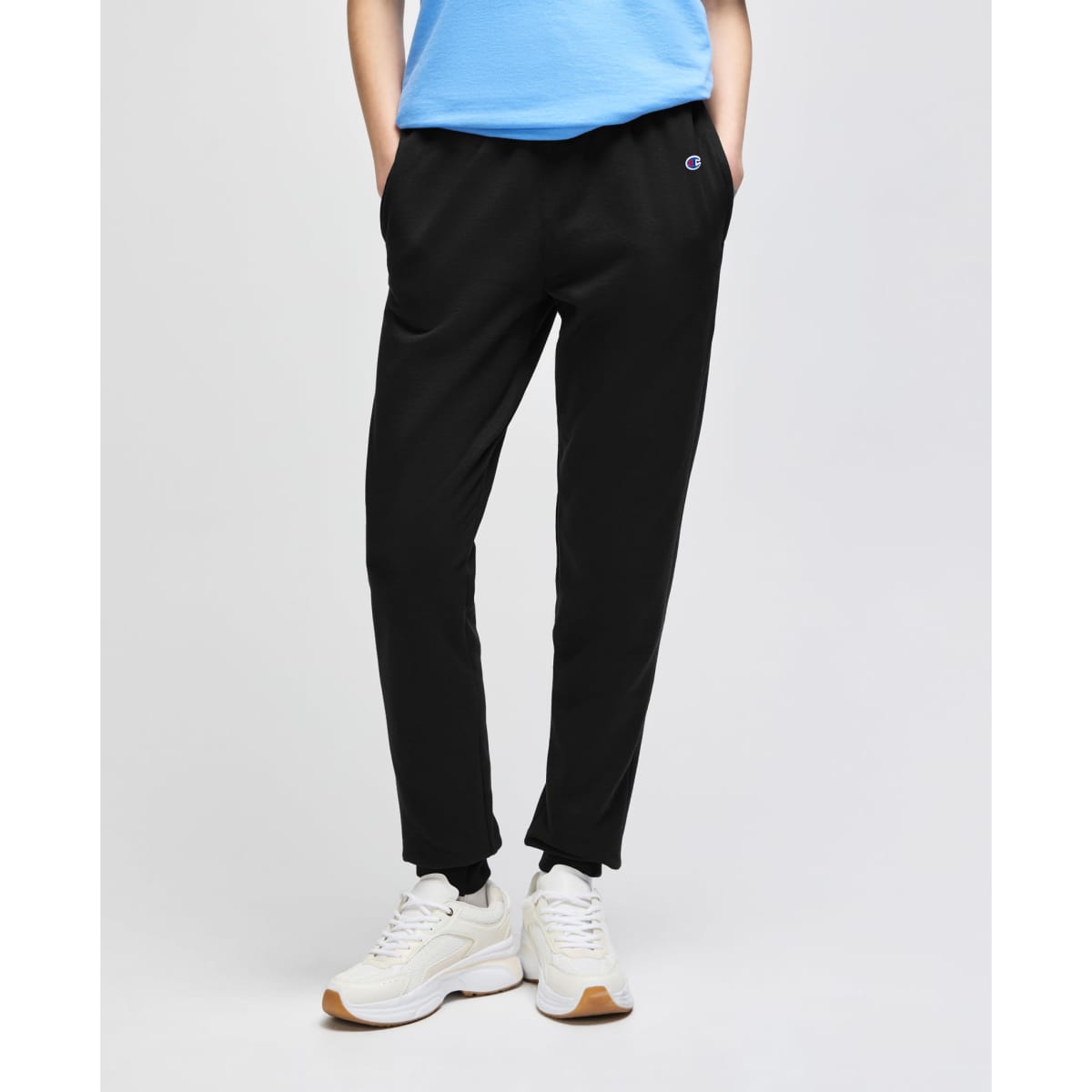 A pair of black fleece jogger pants with side pockets, styled with a light blue top and white shoes.