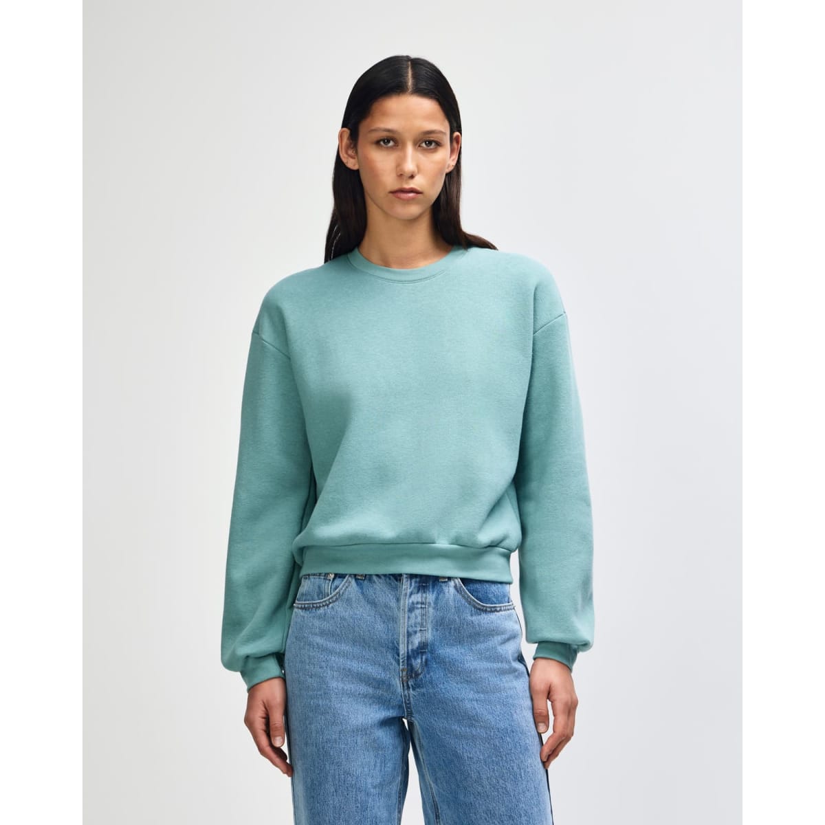 A women's crewneck sweatshirt in a soft teal colour, featuring long sleeves and a relaxed fit. It has a logo.