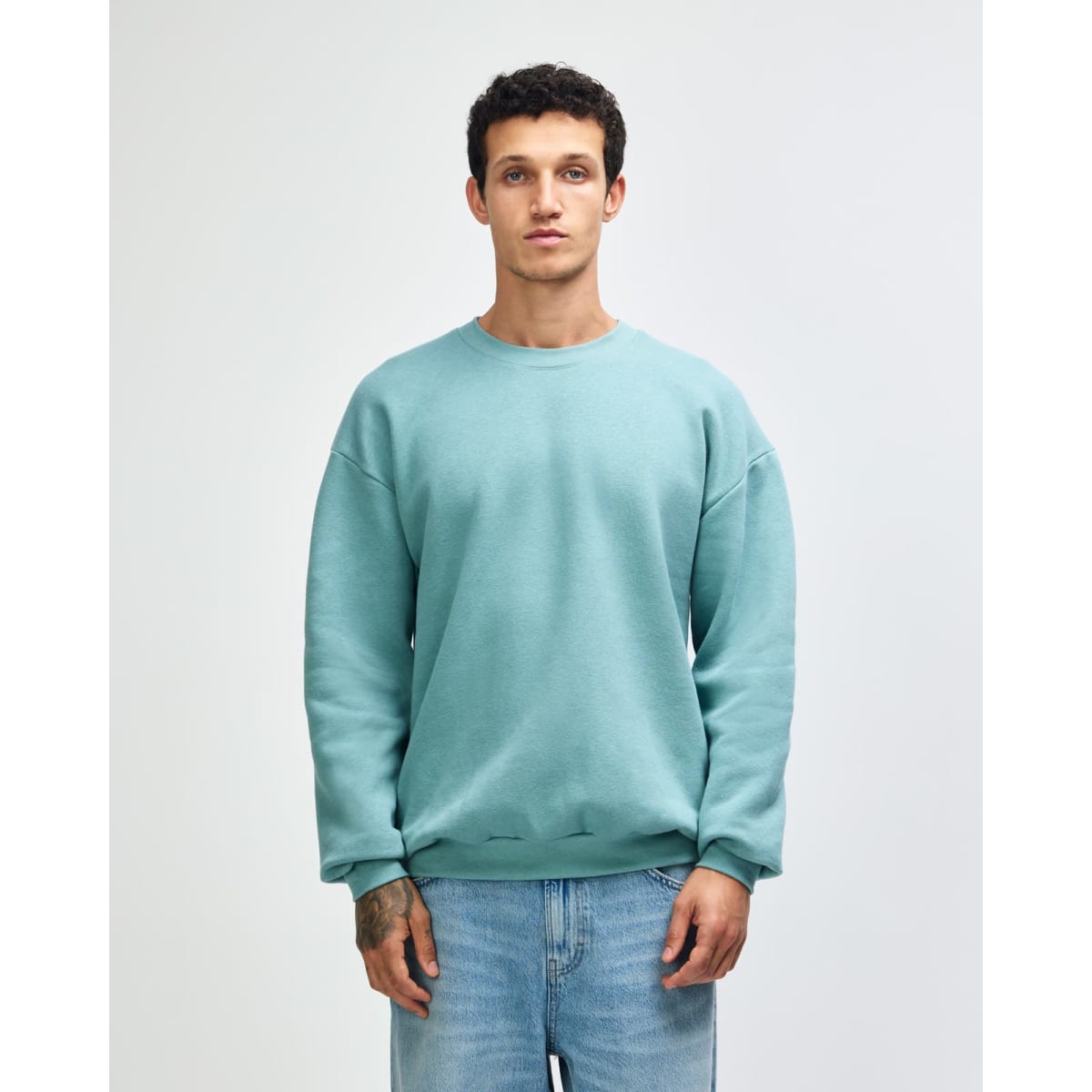 A unisex crewneck sweatshirt in a soft green hue, featuring long sleeves and relaxed fit. Contains branding.