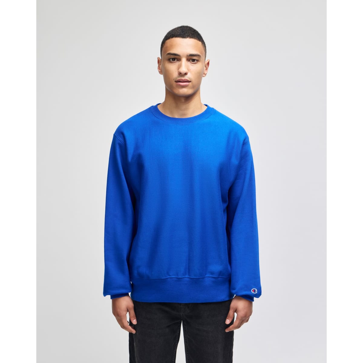 A blue adult crew sweatshirt featuring a logo, displayed on a model against a plain background.