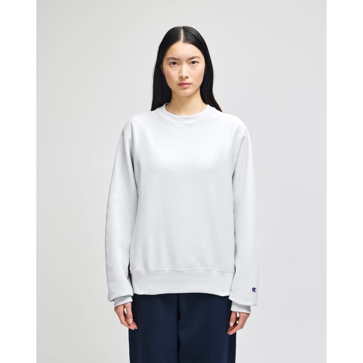 A grey Champion Reverse Weave® adult crew sweatshirt worn by a model, featuring a branding logo.