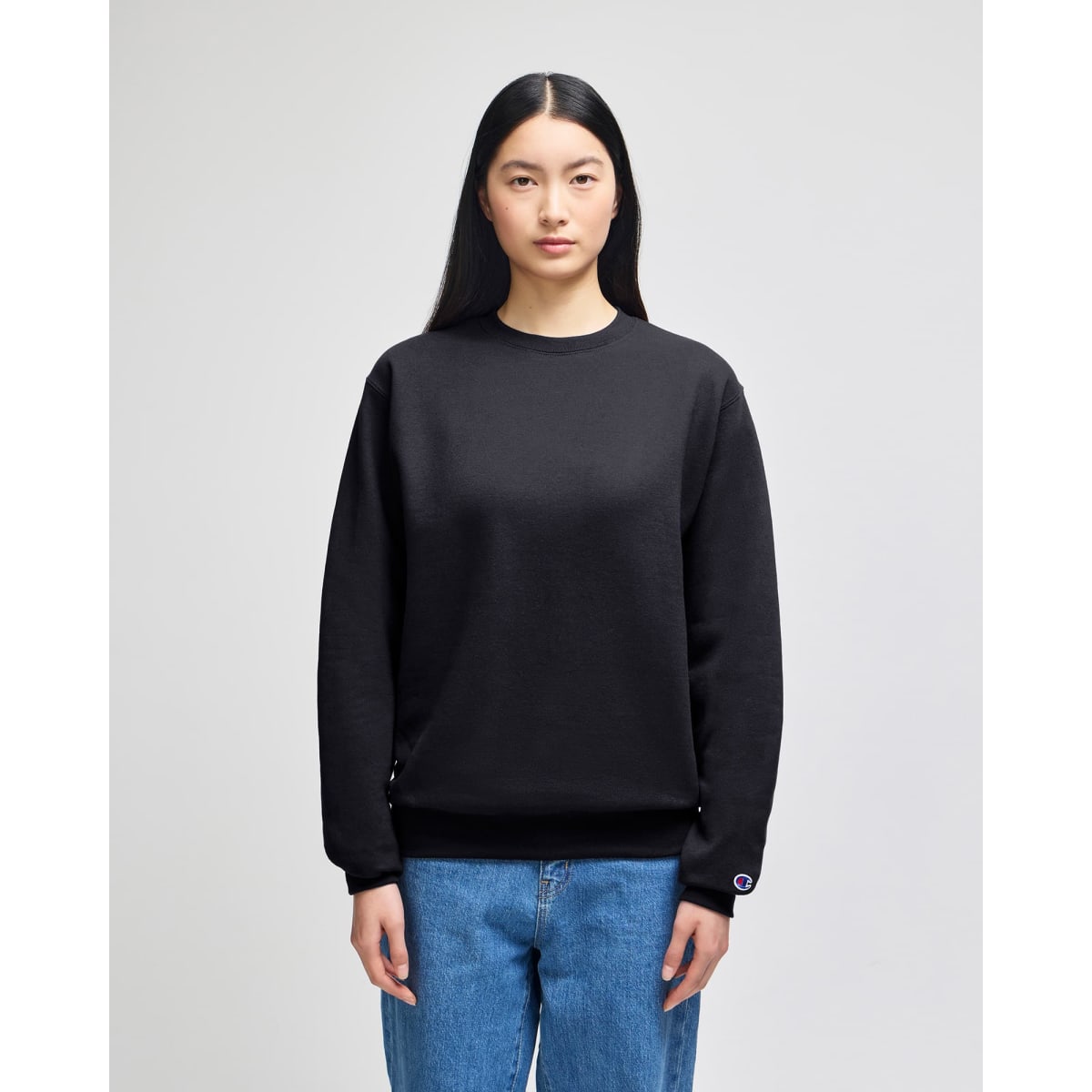 A black crewneck sweatshirt with long sleeves and a logo on one sleeve, displayed on a model.
