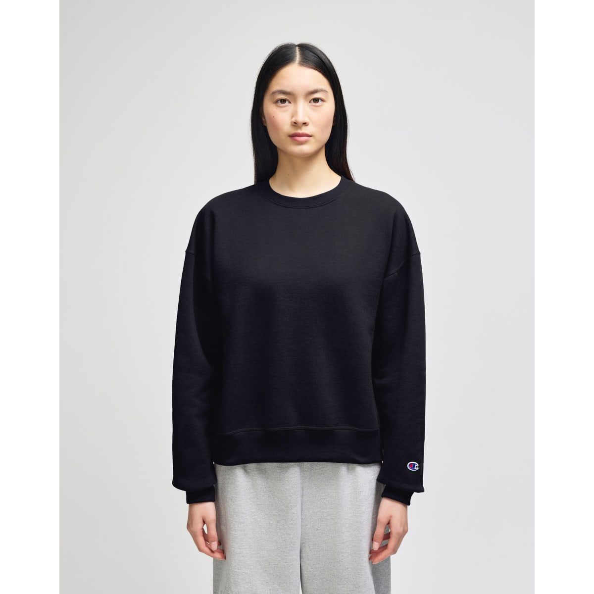 A black women's crewneck sweatshirt with a relaxed fit, featuring a small logo on the sleeve.