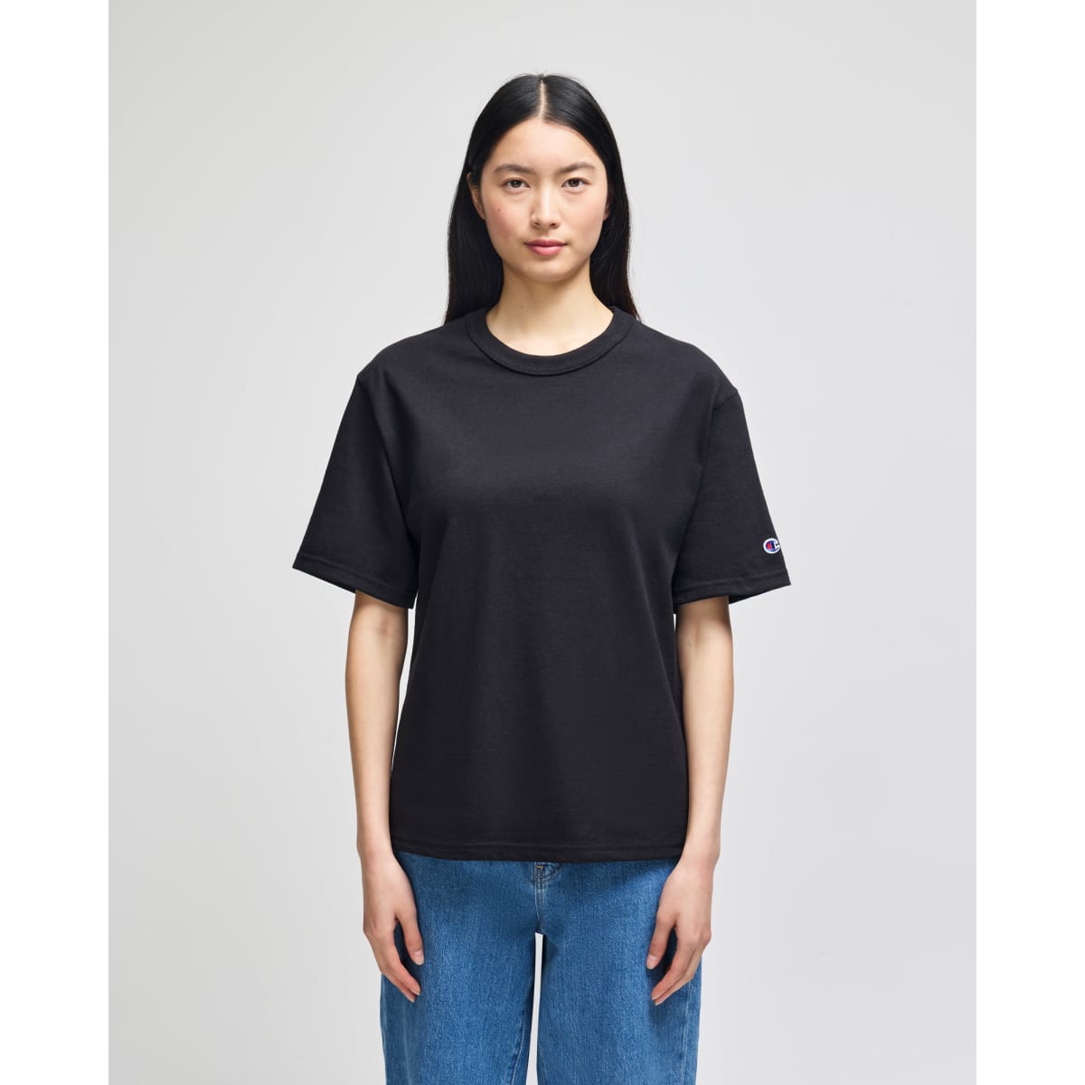 A black Champion Adult Heritage Jersey T-Shirt displayed on a model, featuring a logo on the sleeve.