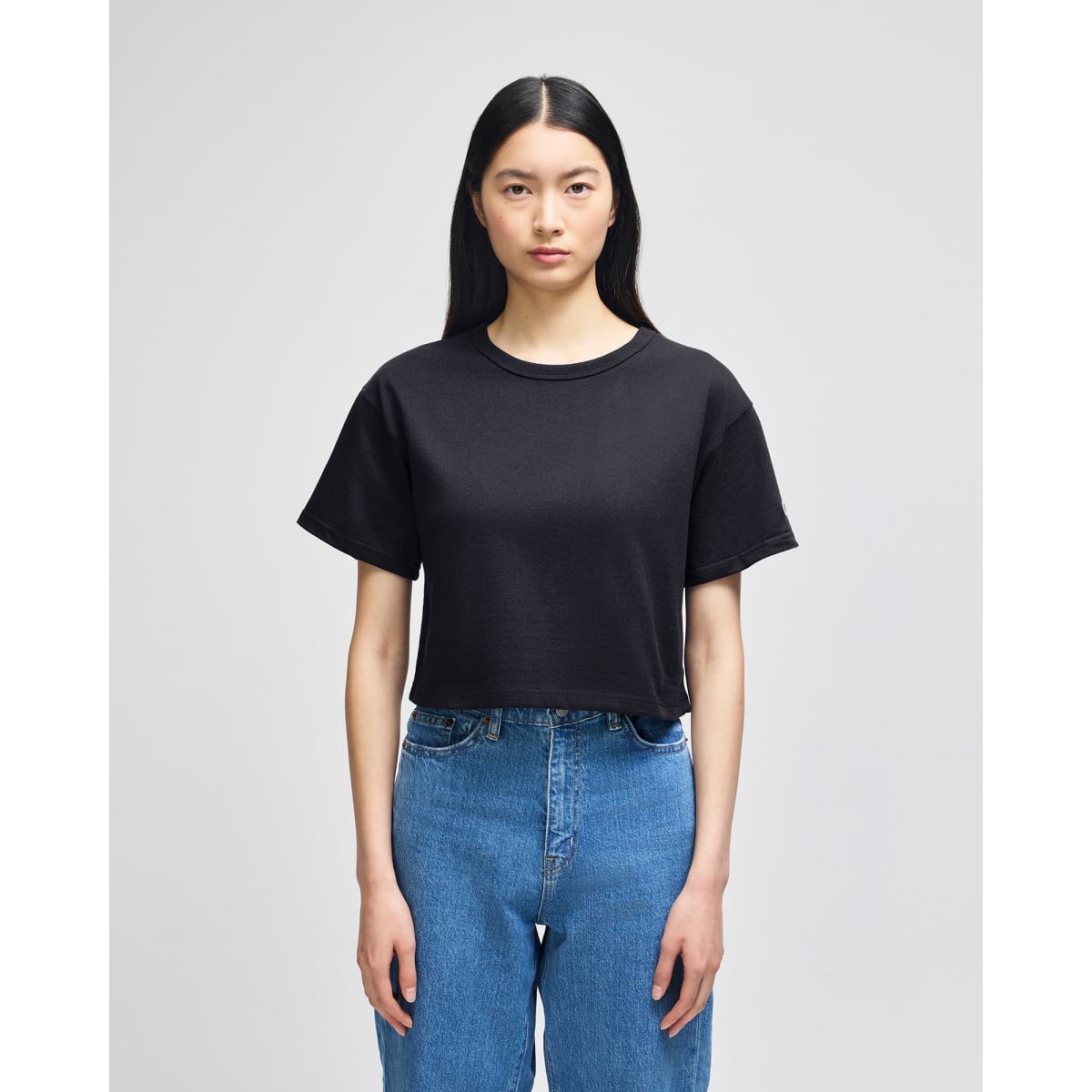 A black cropped short sleeve jersey t-shirt featuring a casual fit, displayed on a model wearing blue jeans.