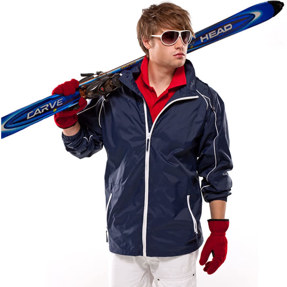 A man in a navy jacket holds skis, wearing red gloves and sunglasses, with a casual outfit underneath.