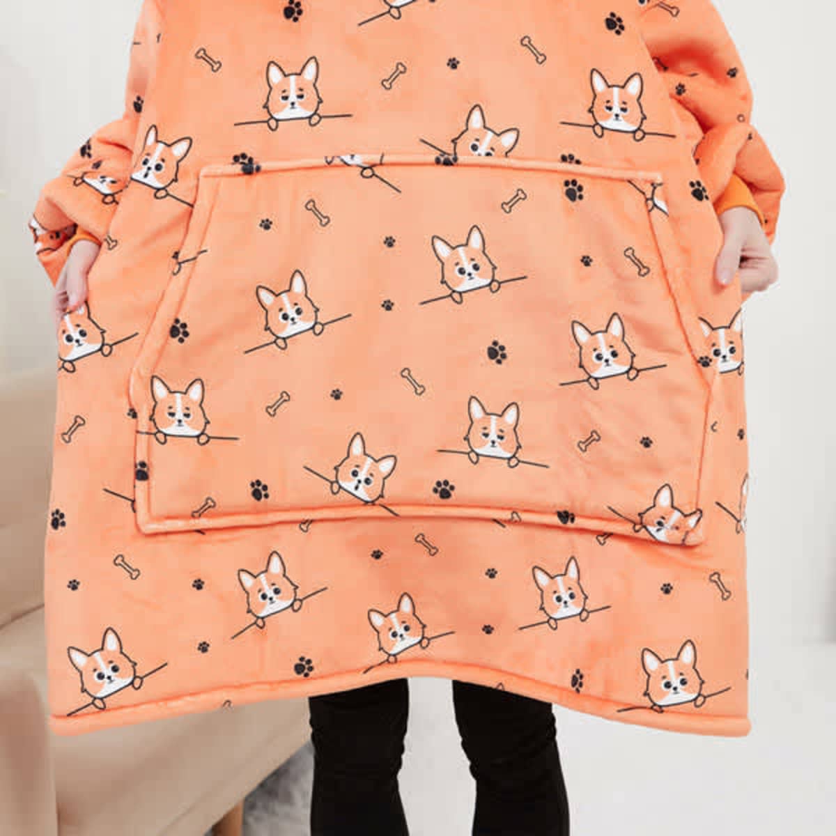 An orange flannel hoodie blanket featuring a cute corgi and bone pattern, with a large front pocket.