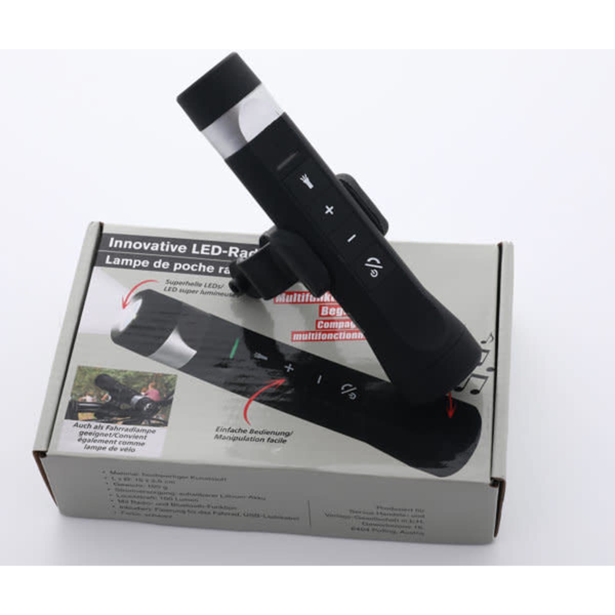 A portable black LED light torch with a speaker, resting on its packaging. The product features control buttons.