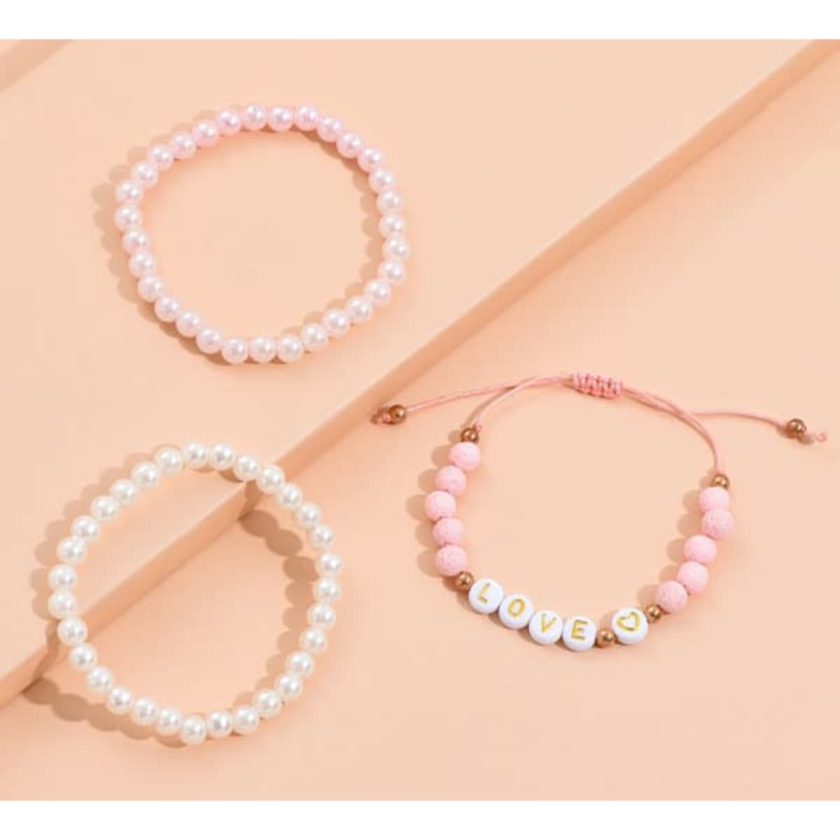 A set of three stretch plastic bracelets in pink and white, featuring decorative beads and a 'LOVE' charm.