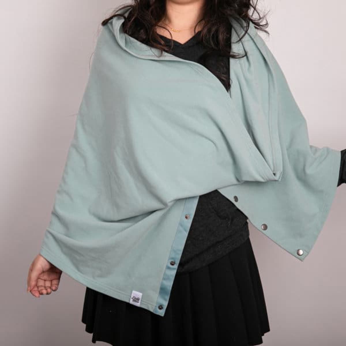 A solid colour button shawl in a soft mint green, featuring buttons for fastening, displayed on a person.