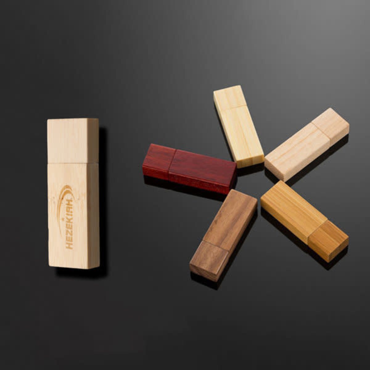 A collection of eight wooden USB memory sticks in various shades, including light, dark, and medium tones, displayed on a dark surface.