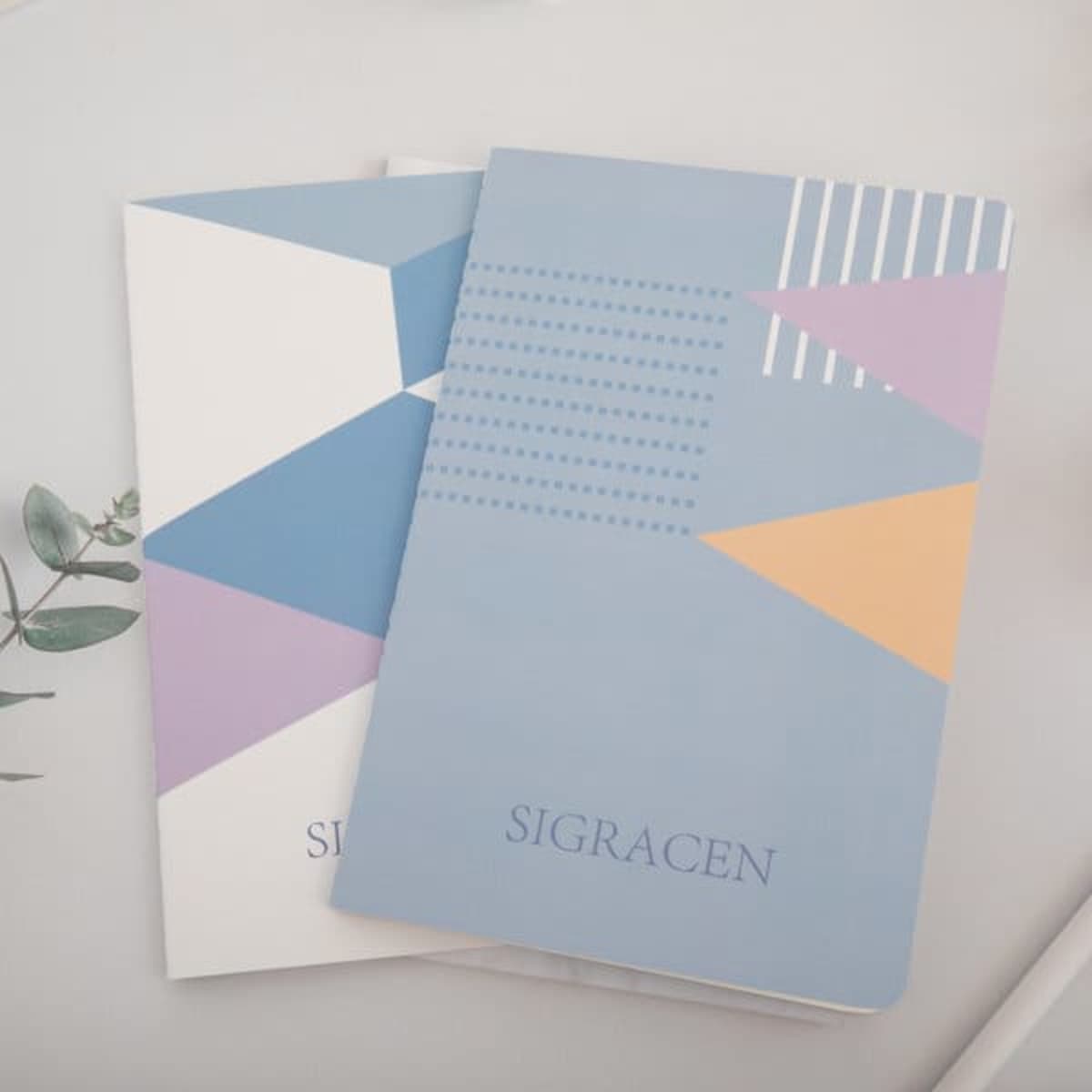 A set of two A5 soft cover ruled notebooks featuring geometric designs in blue, white, purple, and orange, with a logo.