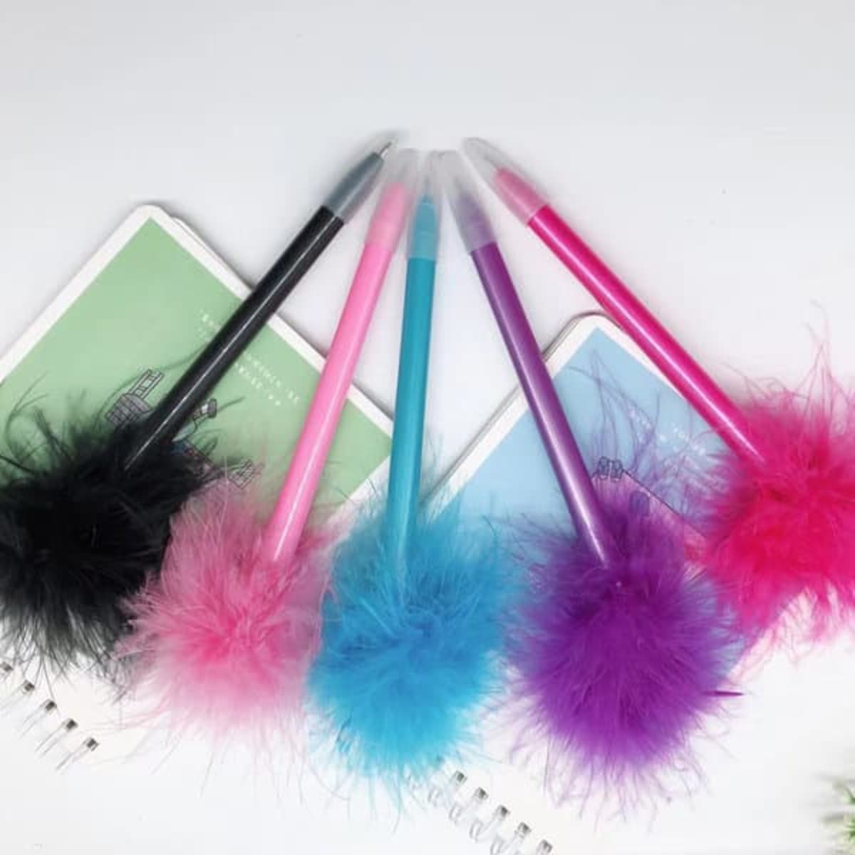A set of five plastic ballpoint pens with cute feather tops in black, pink, blue, purple, and magenta.