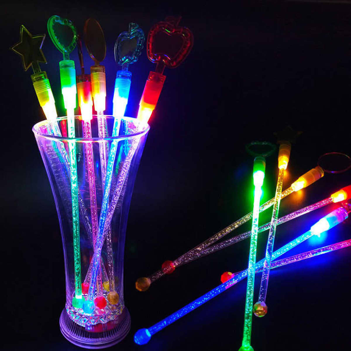 A glass holding multiple colourful LED cocktail stirrers, glowing with various bright lights and designs.