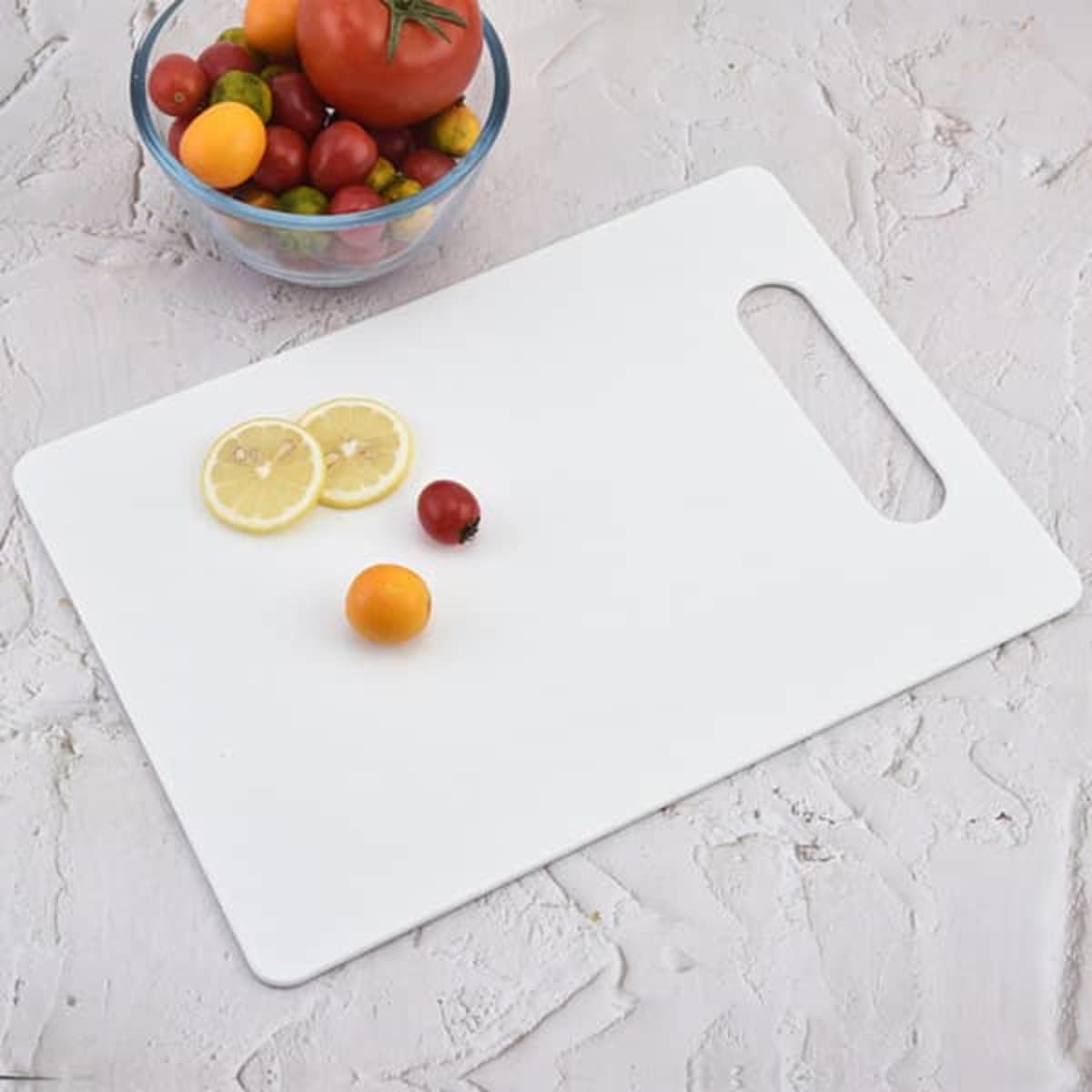 A white plastic cutting board with a grip handle and slices of lemon, beside a bowl of colourful tomatoes.