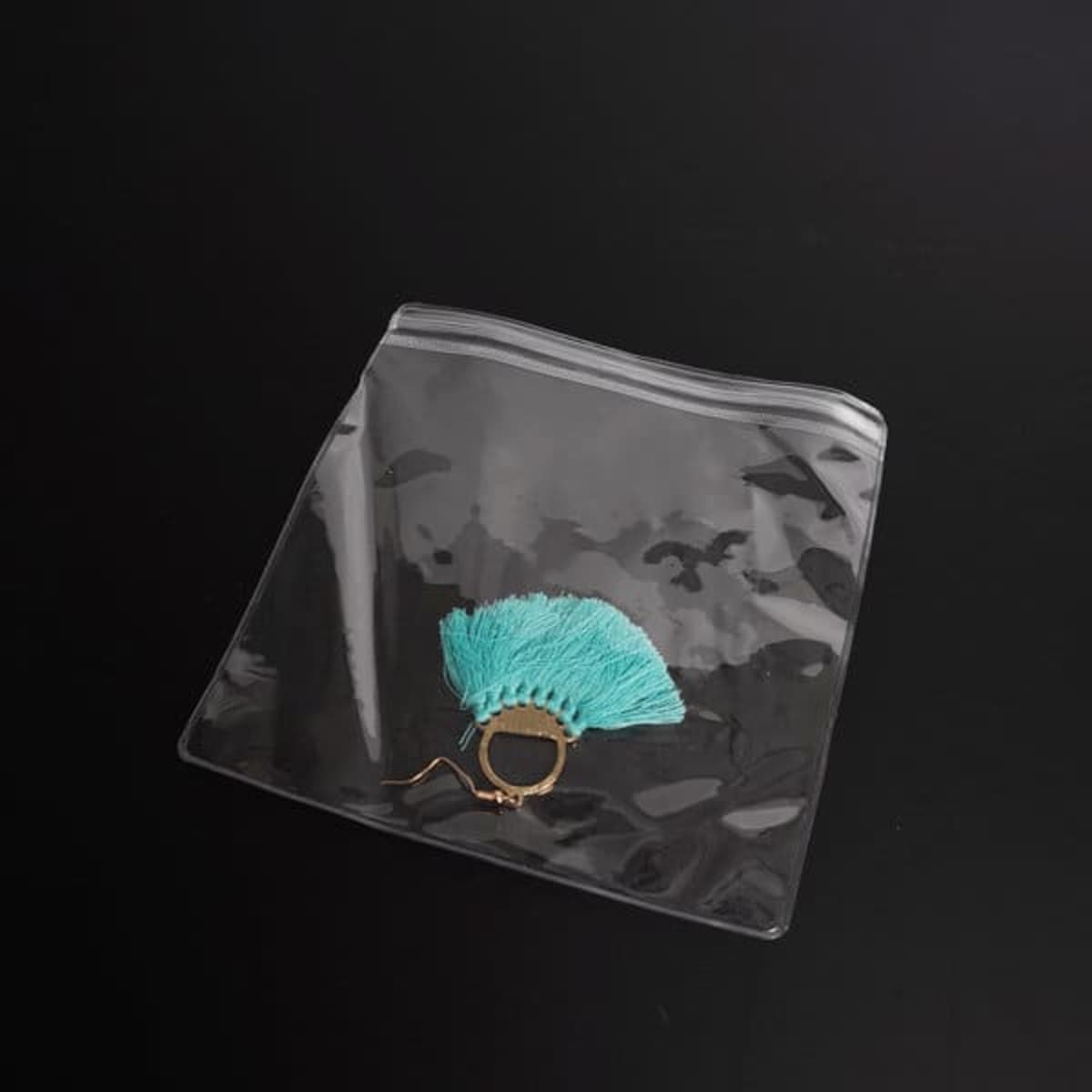 A transparent pouch containing a gold ring adorned with a turquoise tassel, set against a black background.