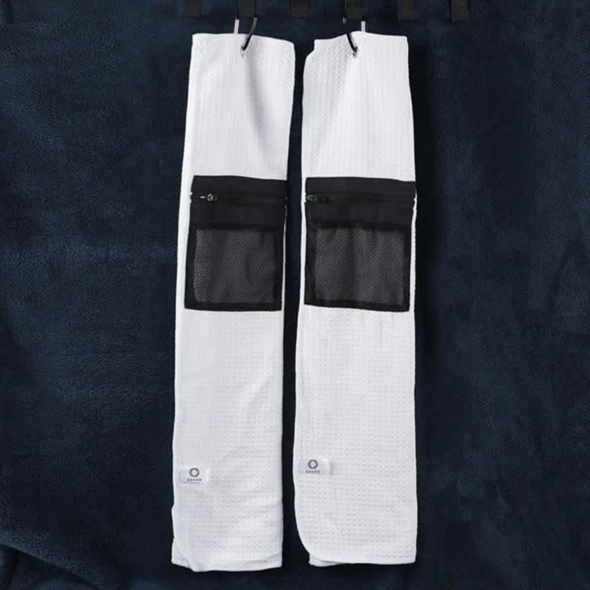 A golf towel in white with a black zippered pocket, featuring a textured fabric. Two towels are displayed together.