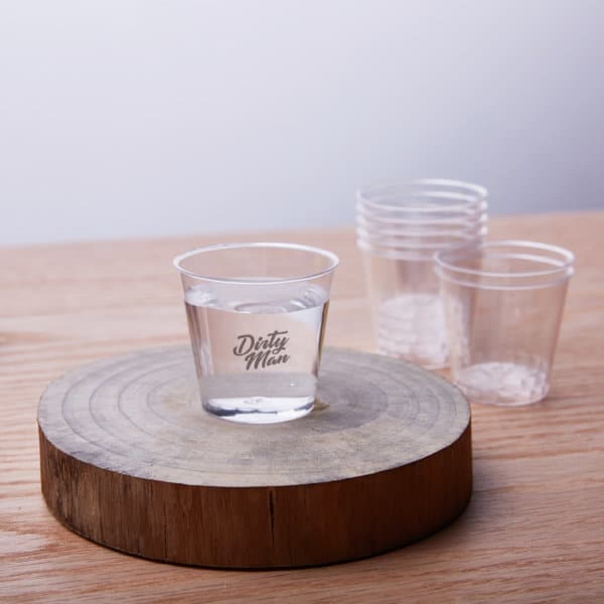 A clear plastic disposable cup with water on a wooden surface, surrounded by additional stacked cups.