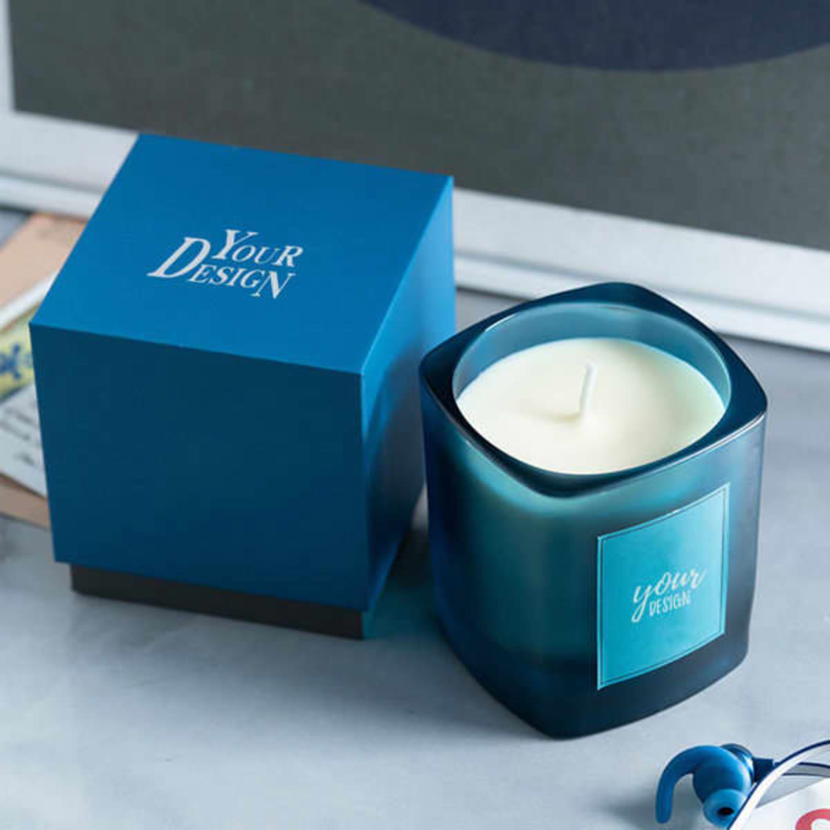 A blue scented candle in a square container with matching packaging, featuring a logo on both.