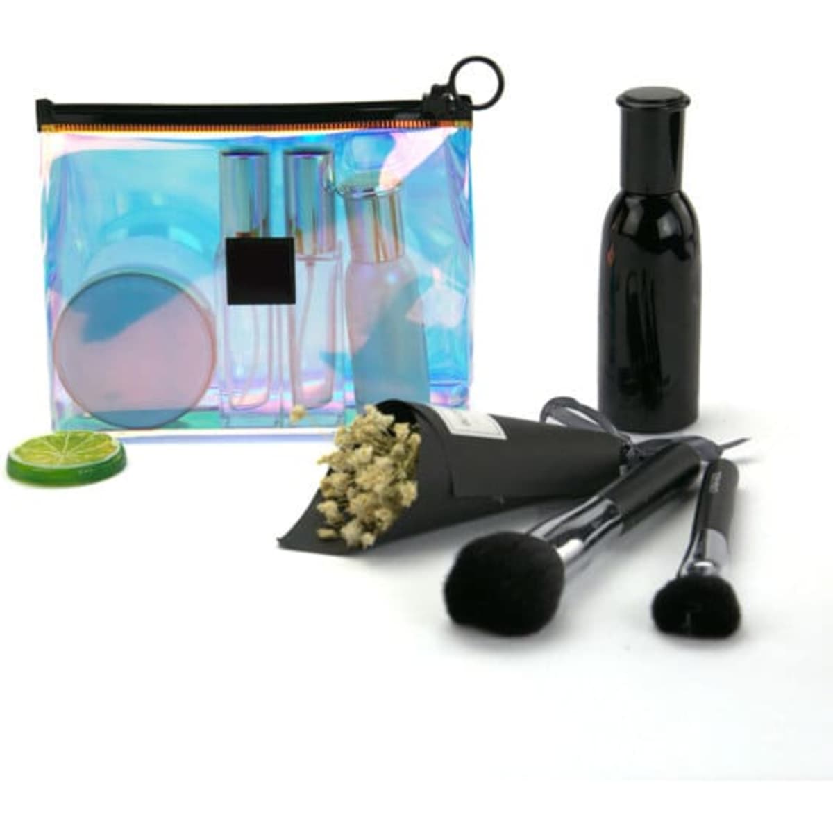 A holographic cosmetic bag with a black logo, containing clear bottles, a compact mirror, brushes, and a lime slice.
